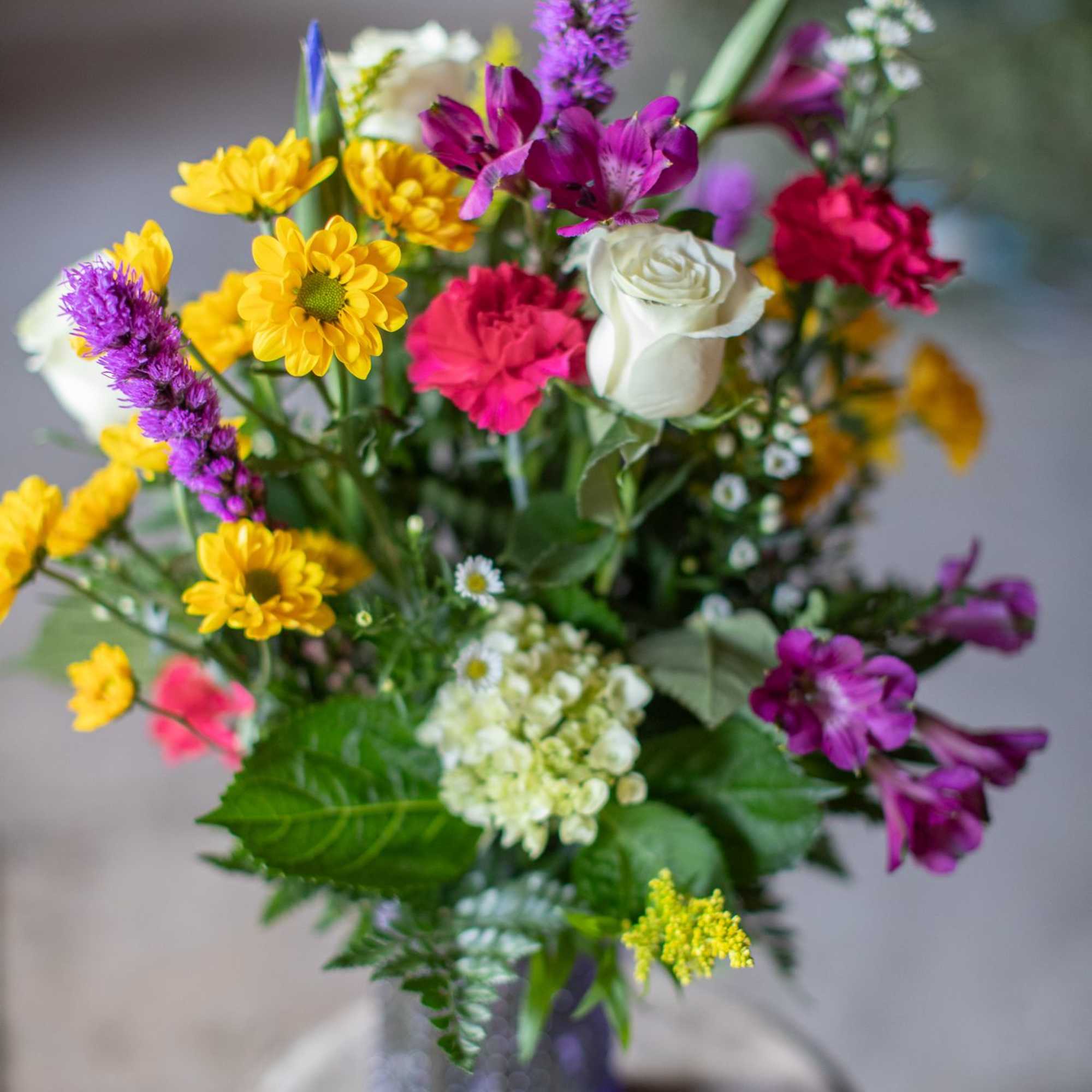 Mixed bouquet with yellow daisies, white roses, and purple flowers in a glass vase
