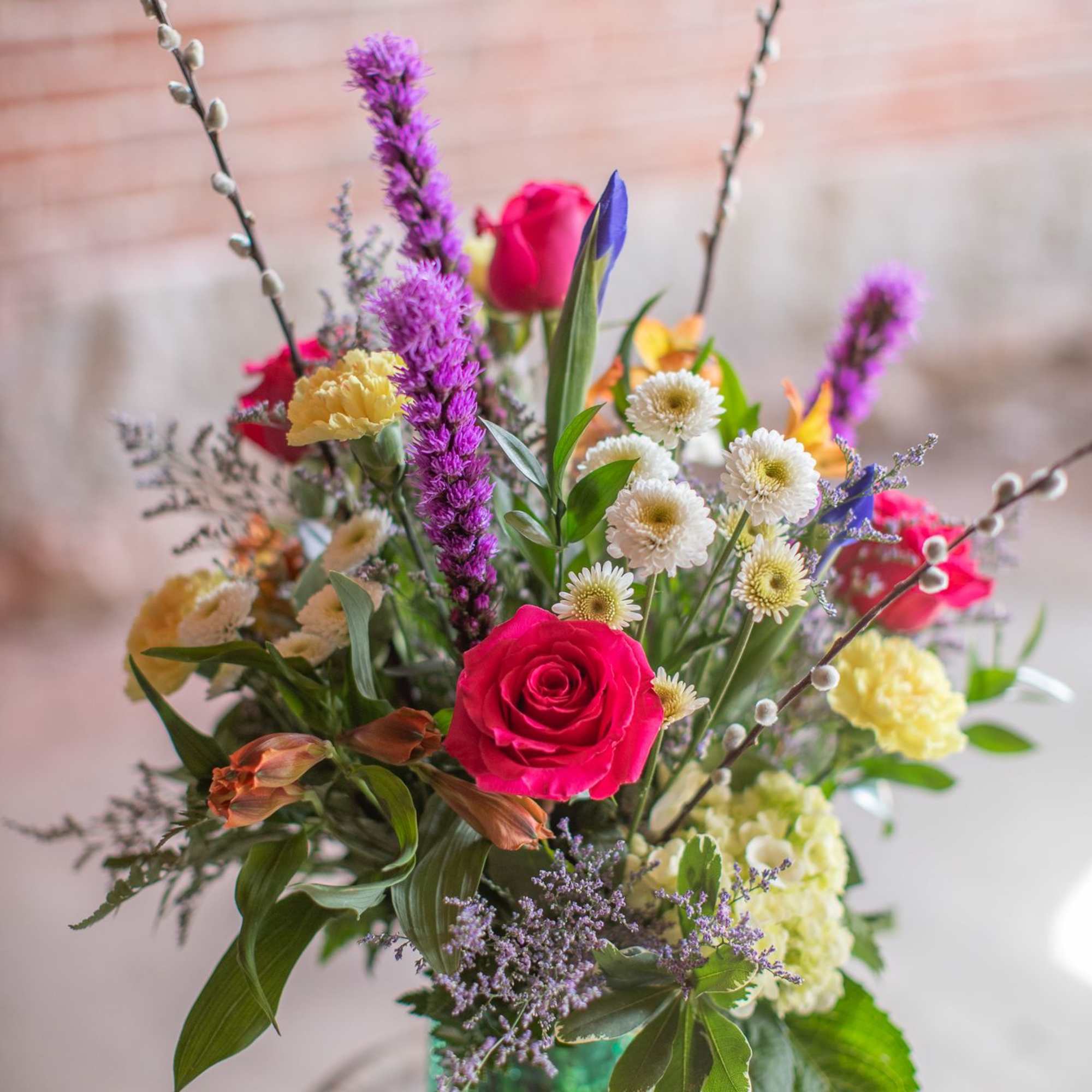 Mixed bouquet in a green glass vase with pink roses and purple spikes