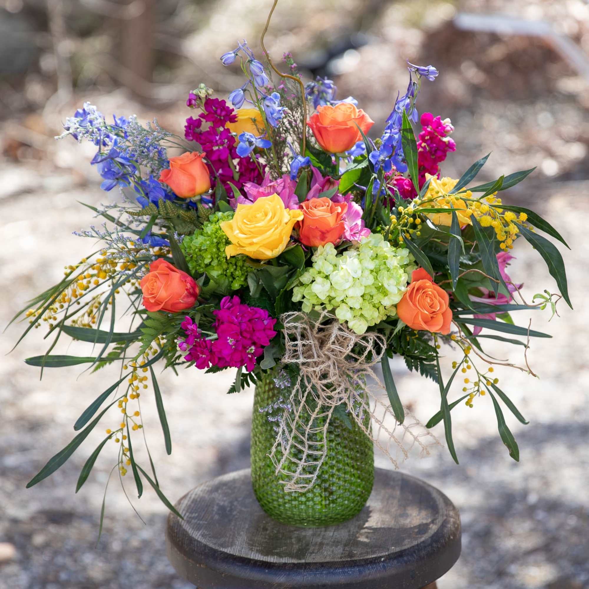 Colorful bouquet of roses, hydrangeas, and blue flowers in a green vase