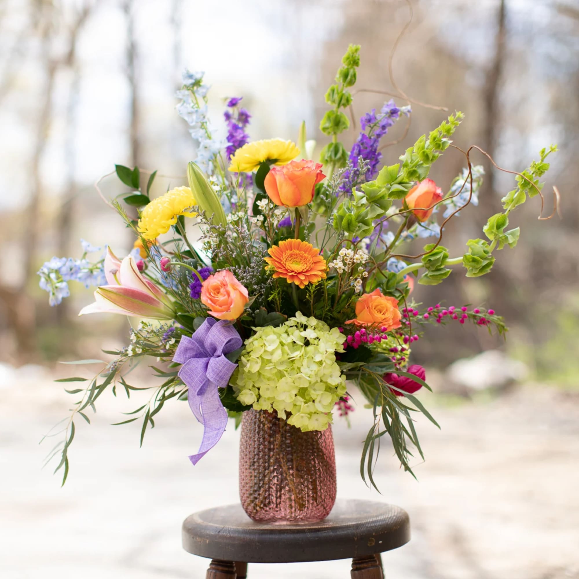 Mixed bouquet in a pink textured vase with a purple ribbon