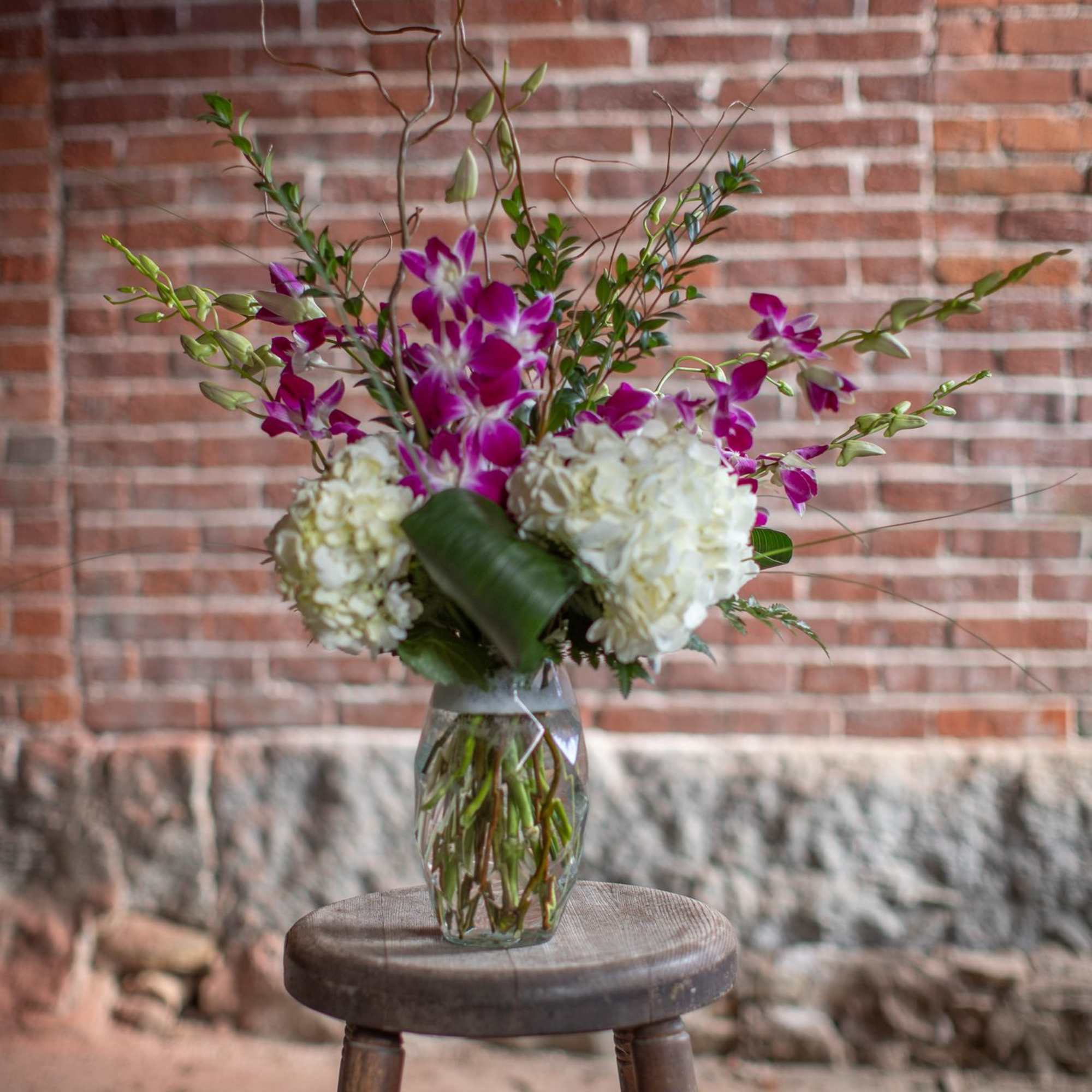 Purple orchids and white hydrangeas in a clear glass vase