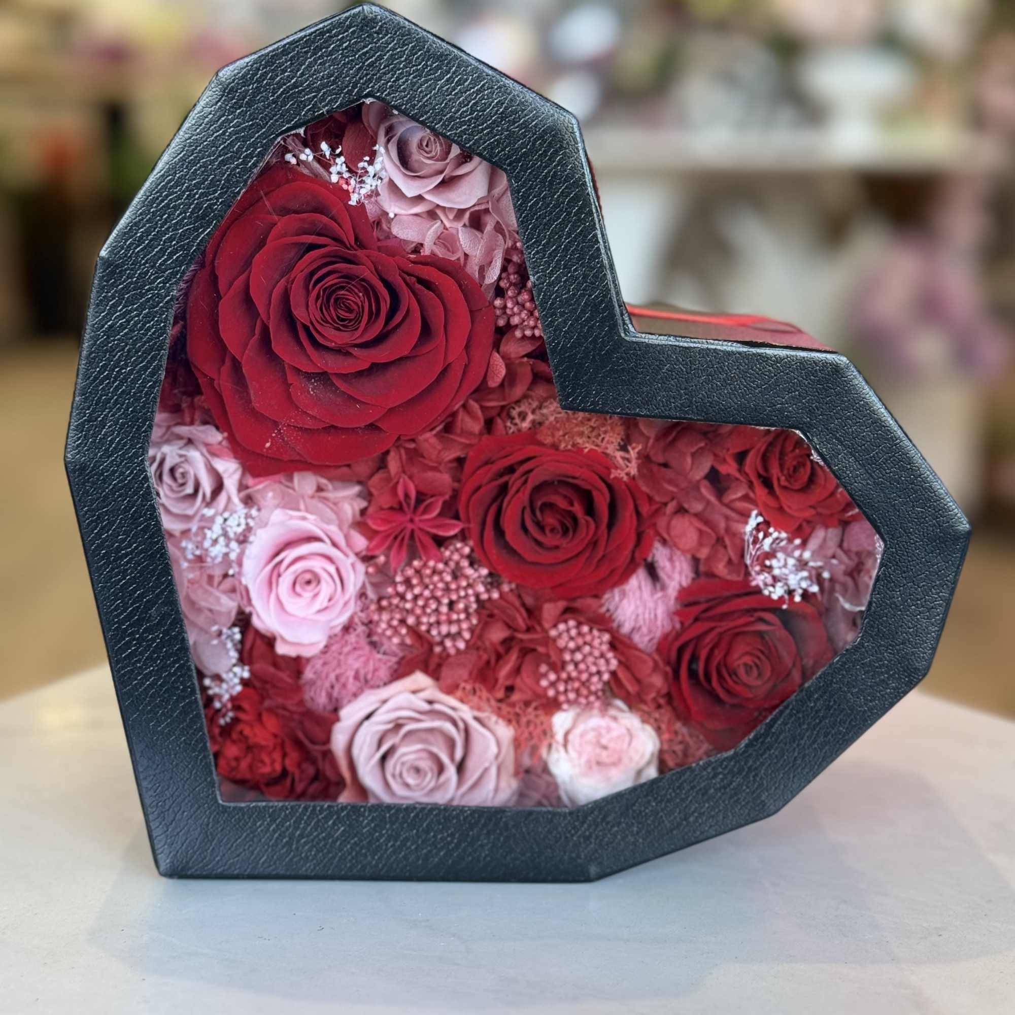 A heart-shaped black gift box reveals a keepsake of preserved roses and