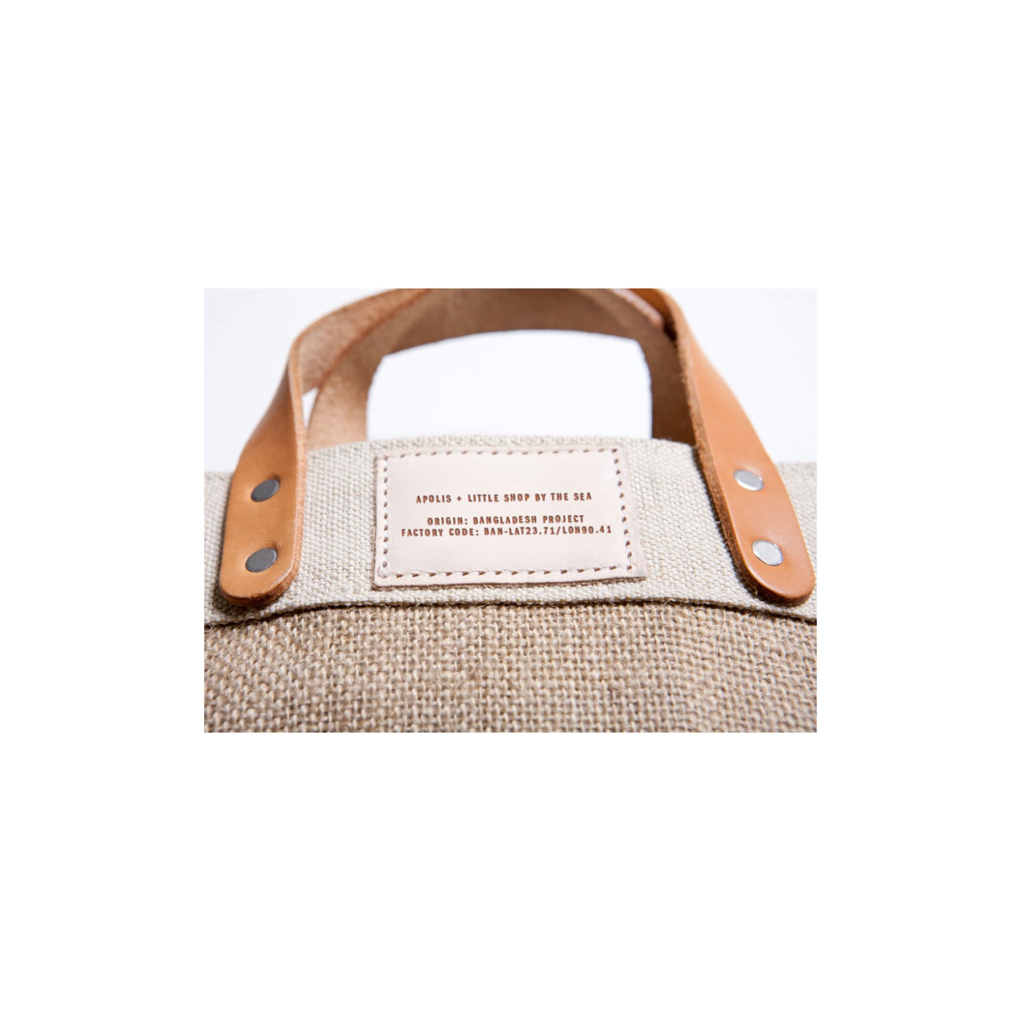 Close-up of a canvas tote bag with leather handles and a stitched label