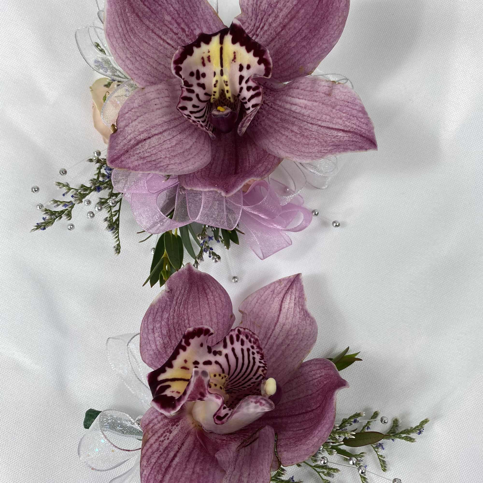 Two purple orchid corsages with ribbon accents on white fabric