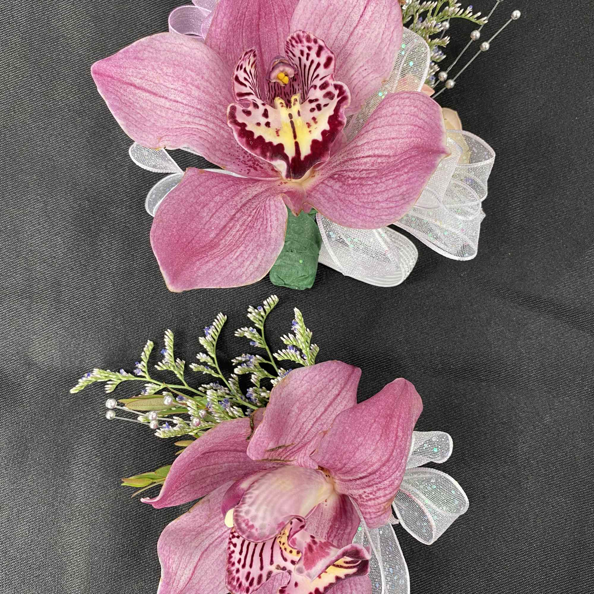 Two pink orchid corsages with white ribbon bows on a dark fabric background