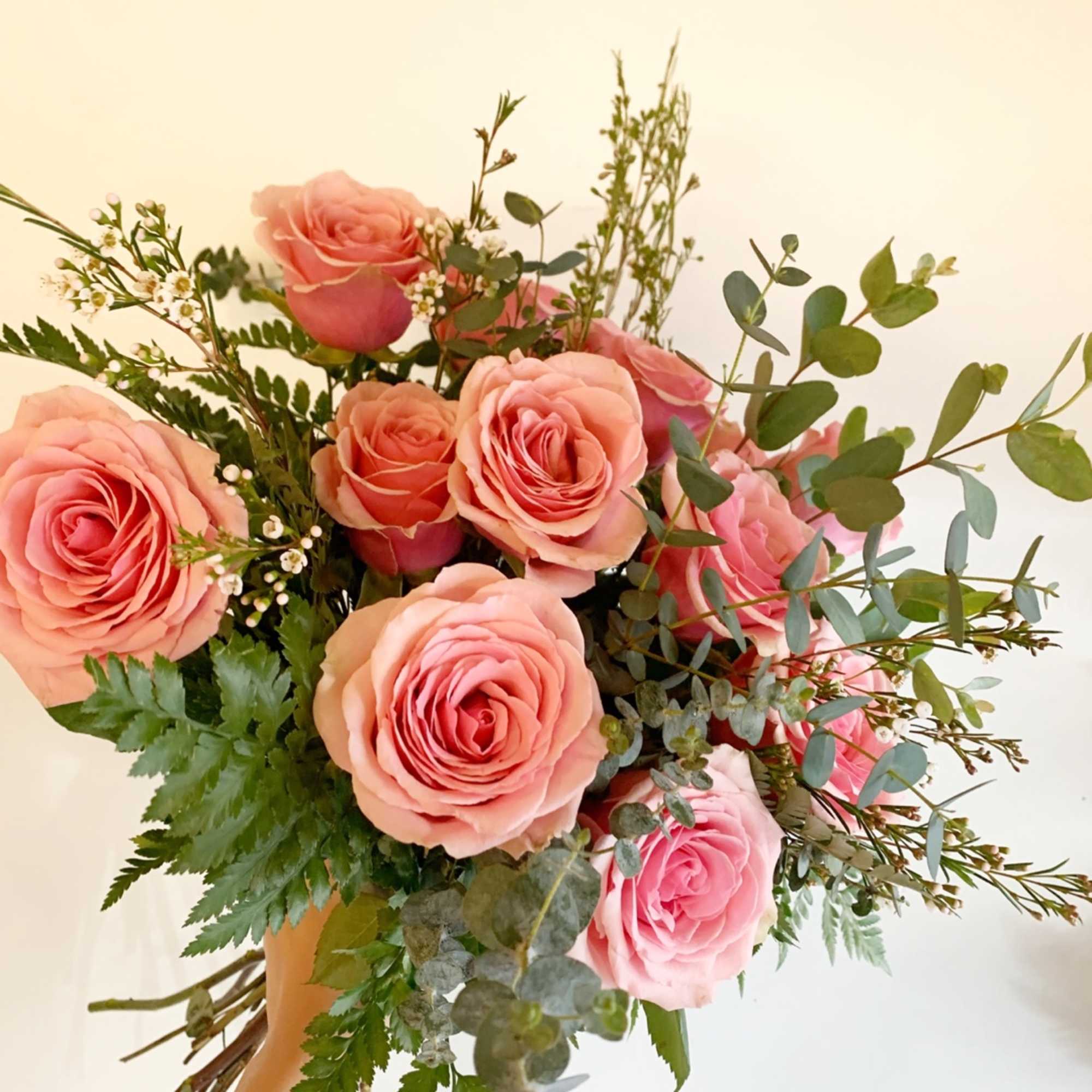 Handheld bouquet of pink roses with mixed greenery