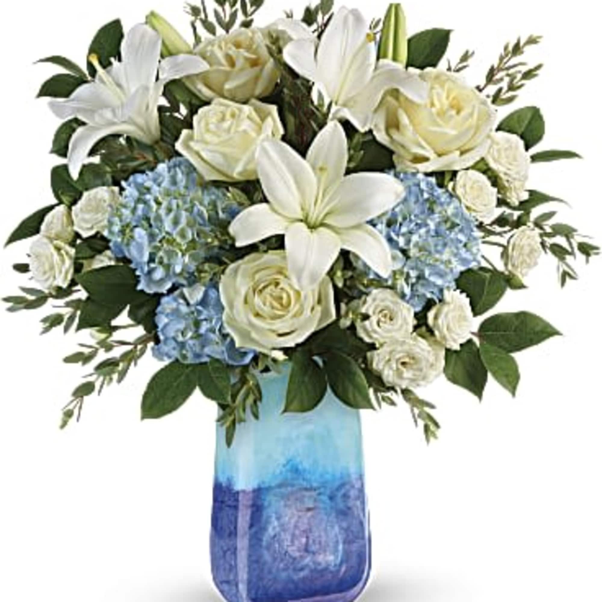White roses, white lilies, and blue hydrangea in a blue vase. 
