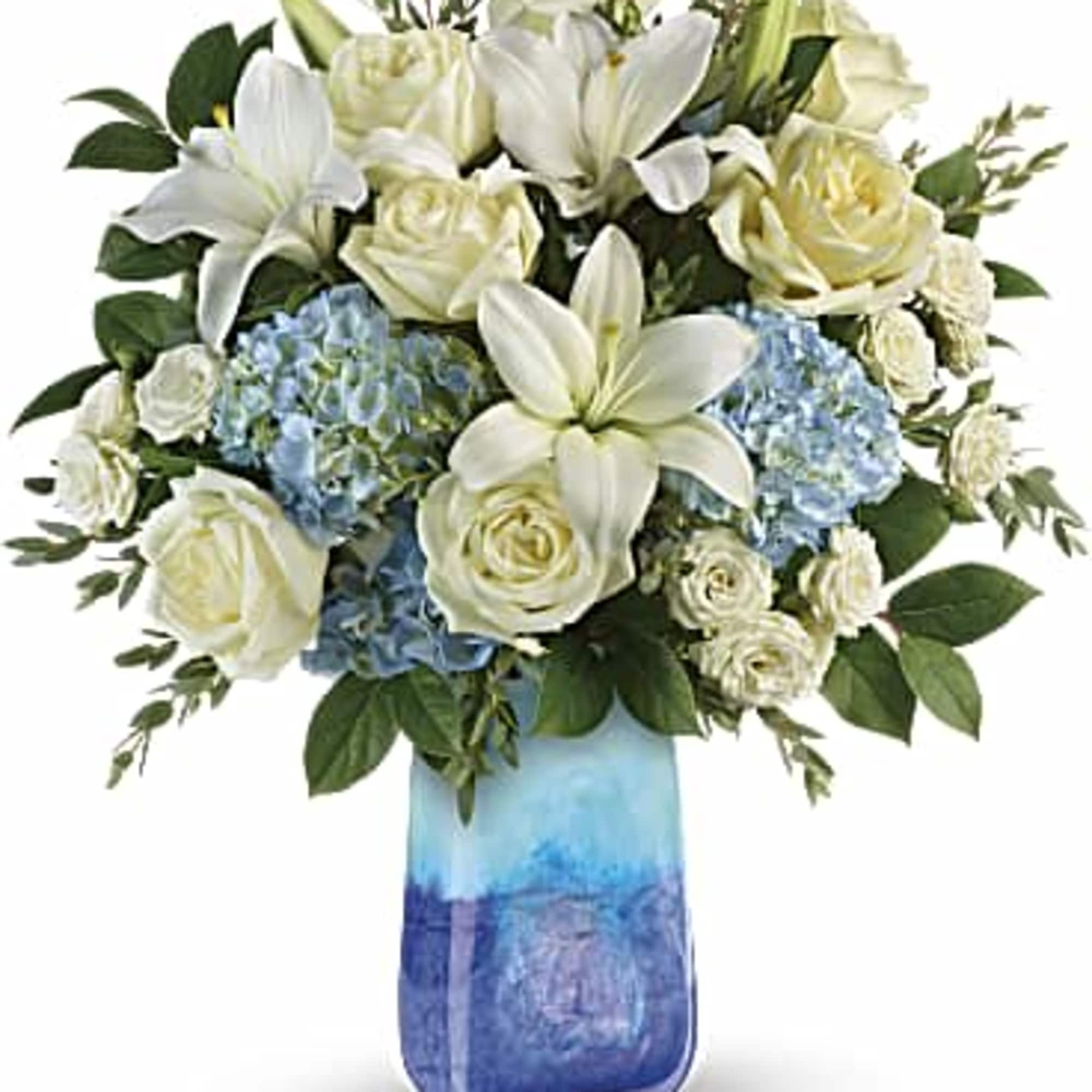 White roses, white lilies, and blue hydrangea in a blue vase. 
