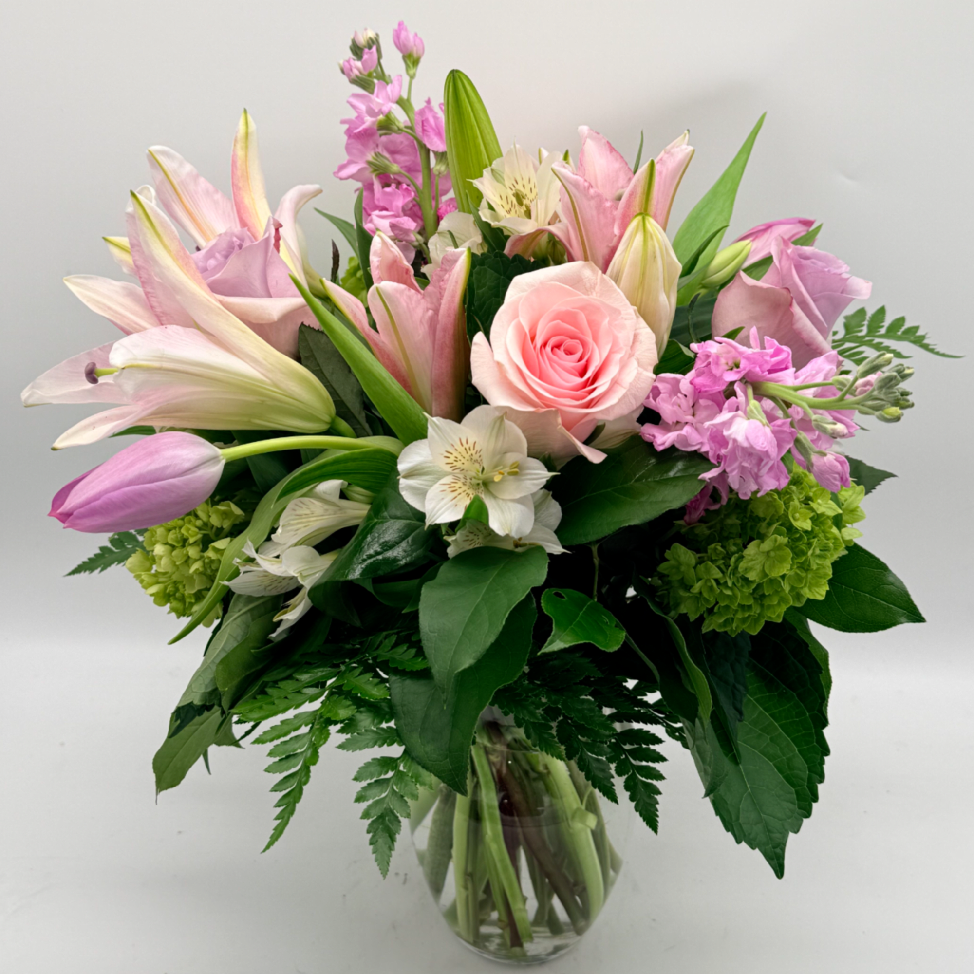 Soft, romantic, and effortlessly graceful, this garden-style arrangement features  lilies, roses