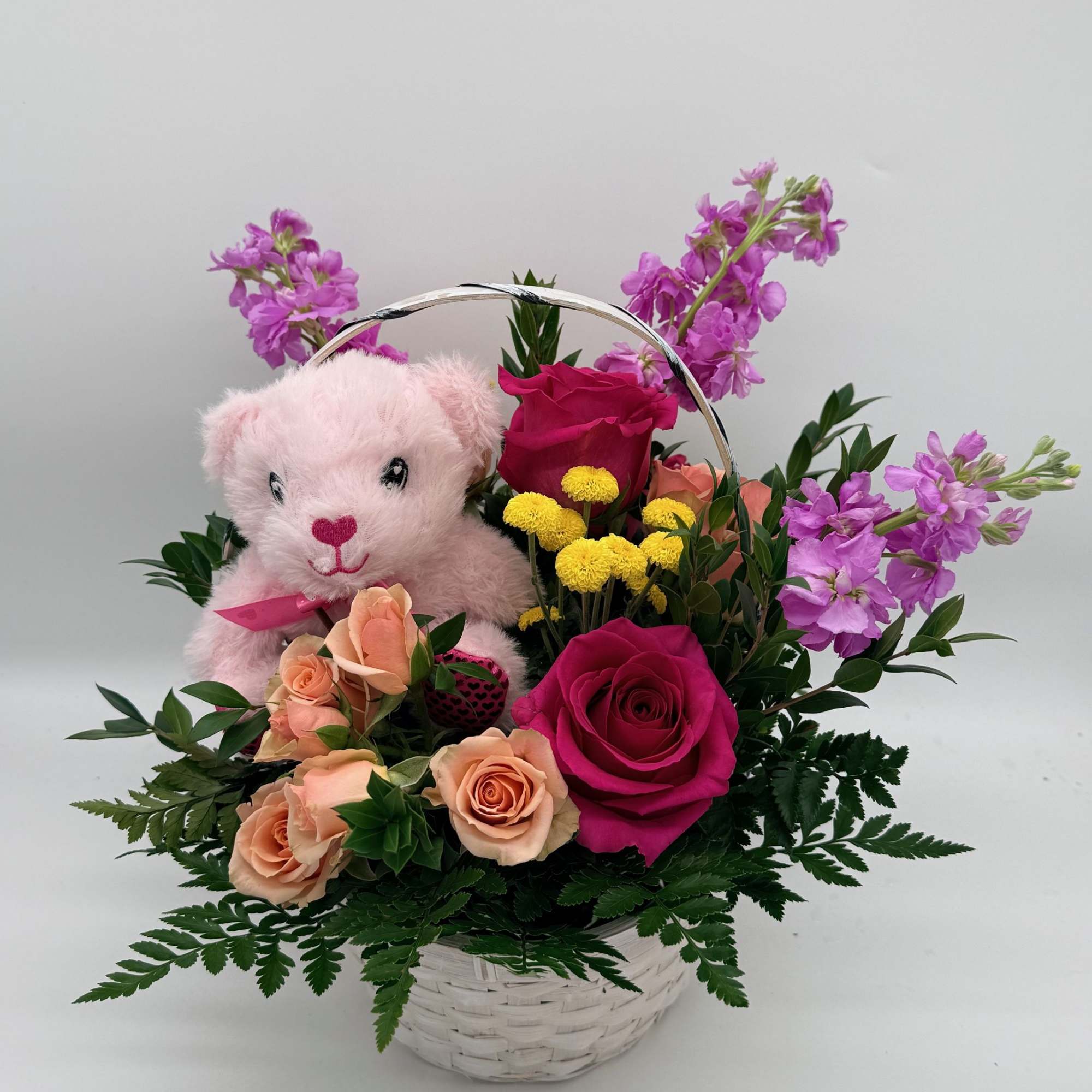 Pink teddy bear in a basket with roses and purple flowers