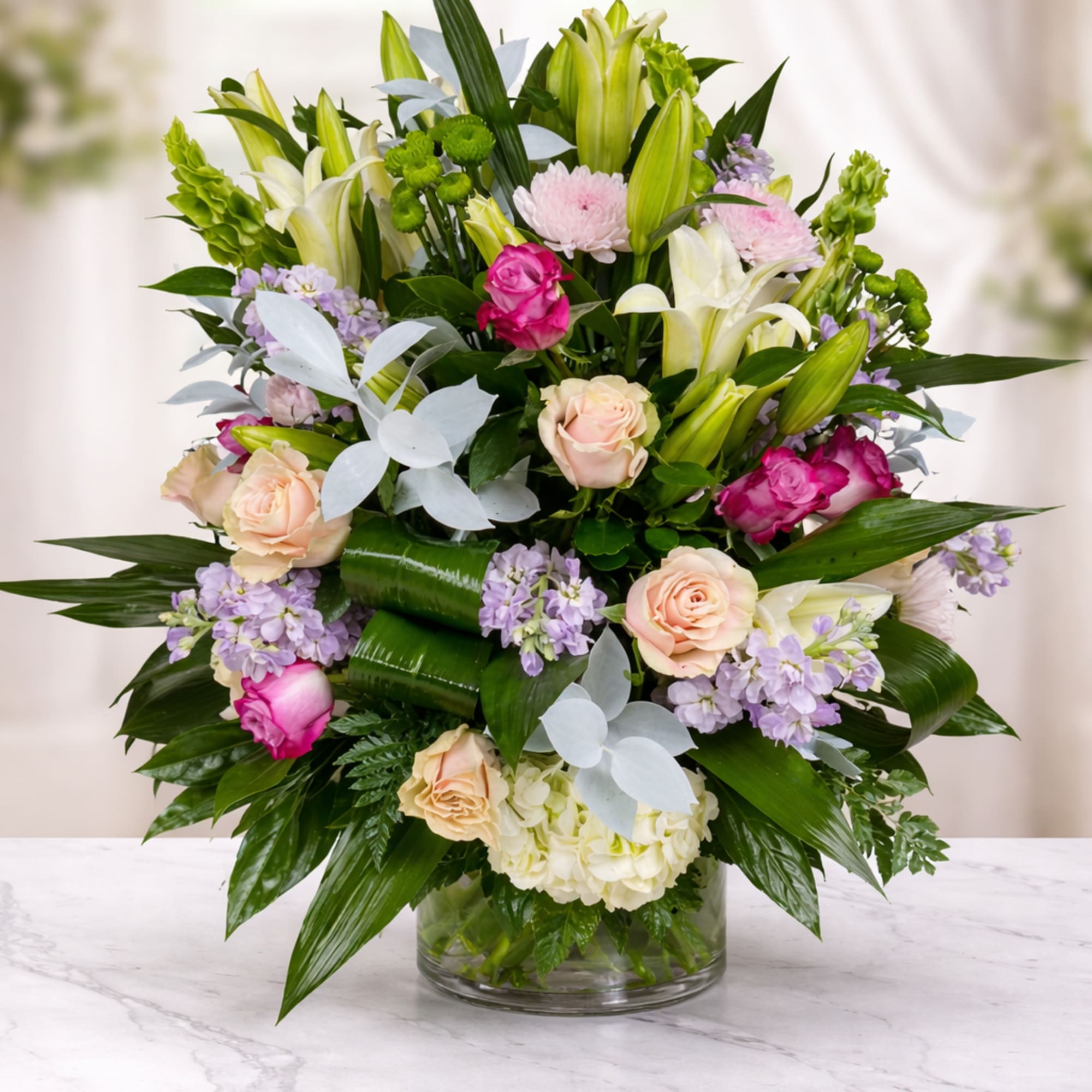 Mixed bouquet of lilies, roses, and lavender flowers in a glass vase