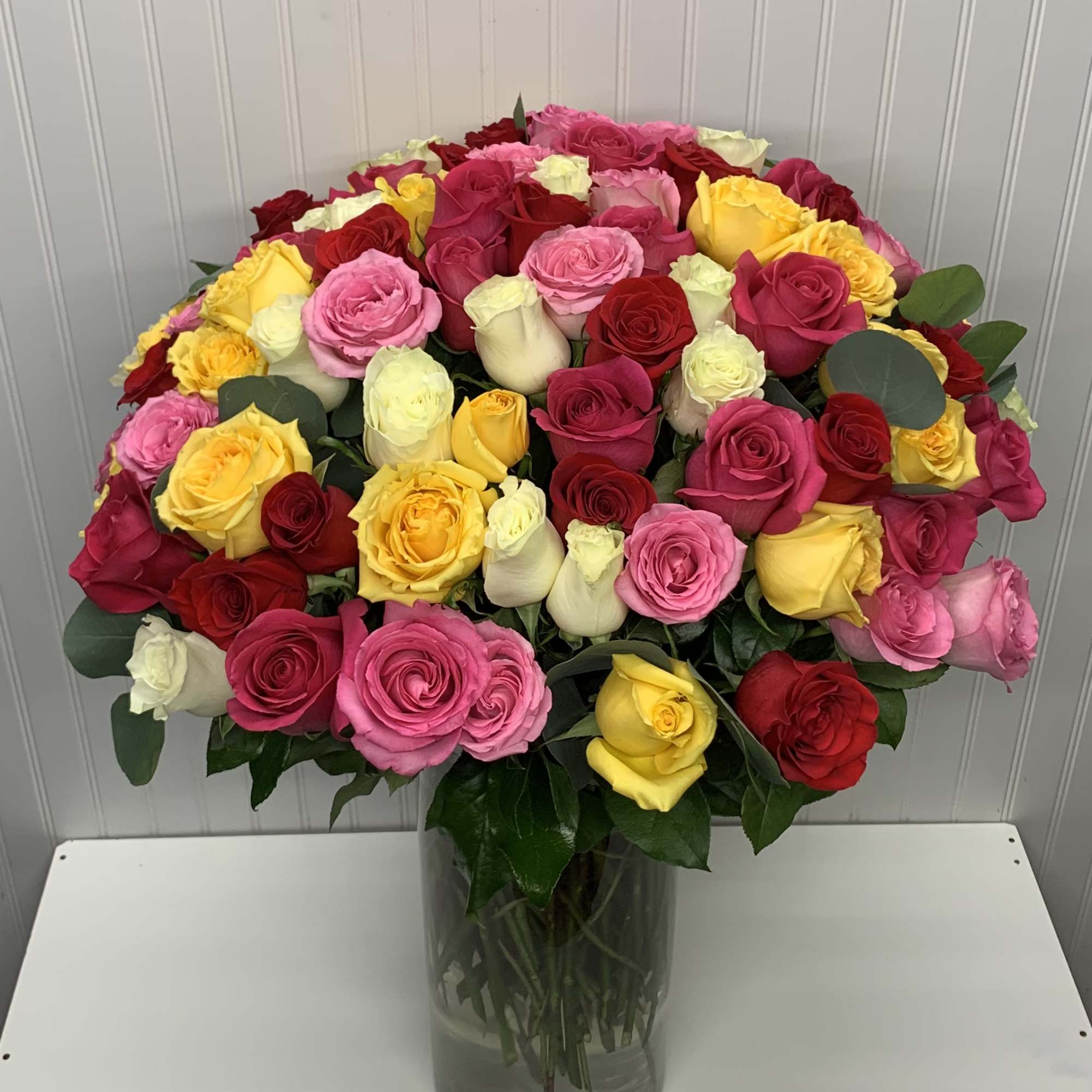 Large mixed bouquet of red, pink, yellow, and white roses in a clear glass cylinder vase