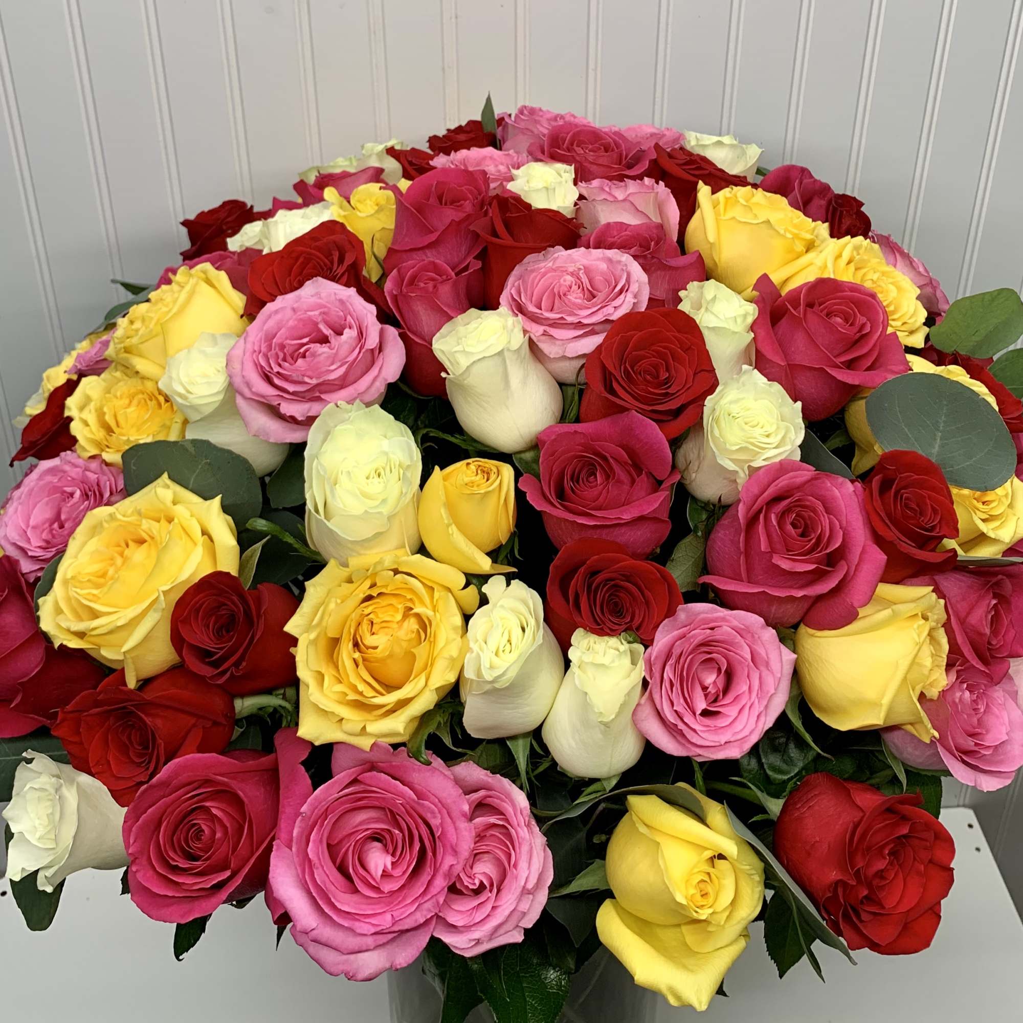 Large arrangement of red, yellow, pink, and white roses in a clear glass vase