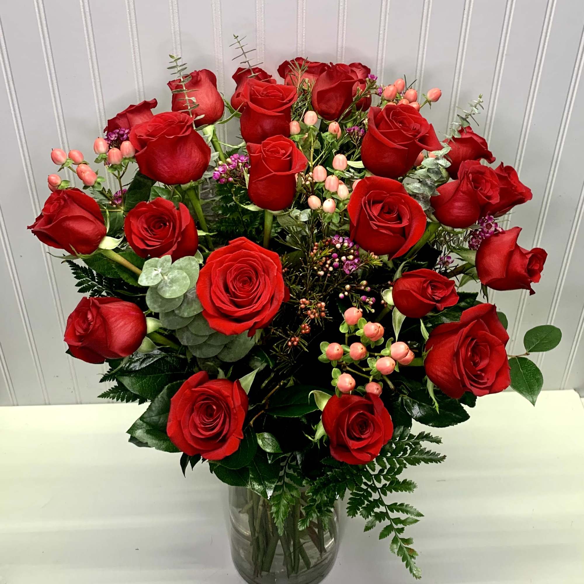 Tall arrangement of red roses with pink berries in a clear glass vase