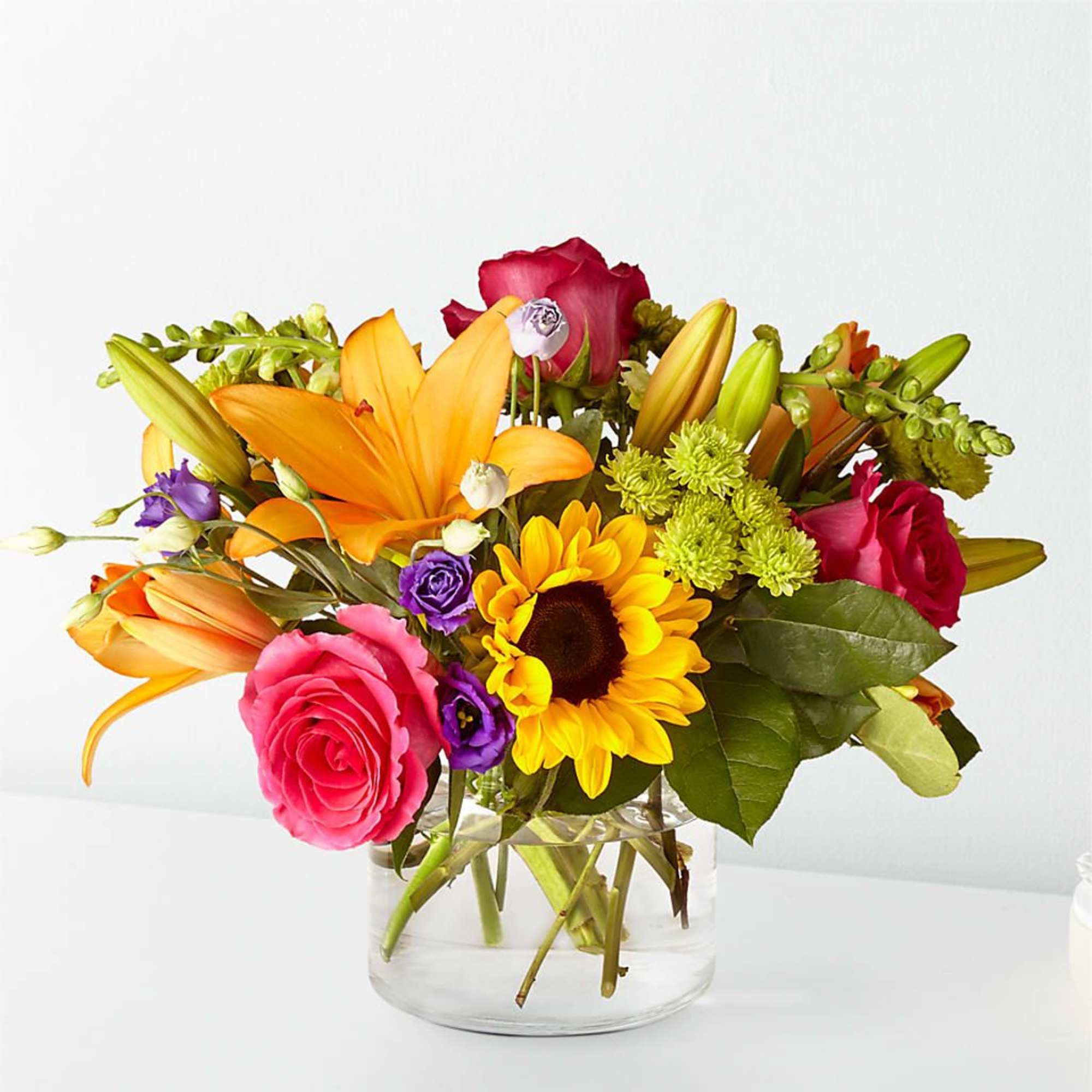Colorful bouquet of roses, lilies, and a sunflower in a glass vase