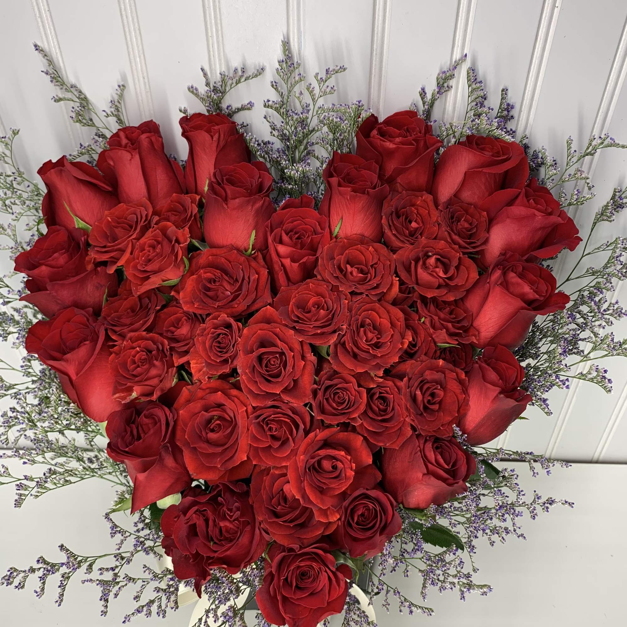 Heart-shaped arrangement of red roses framed with small purple filler flowers.