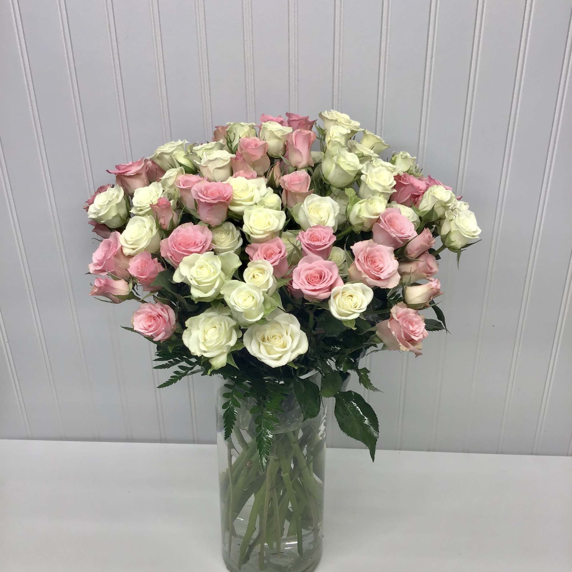 Tall clear vase of light pink and white roses arranged in a full, rounded display