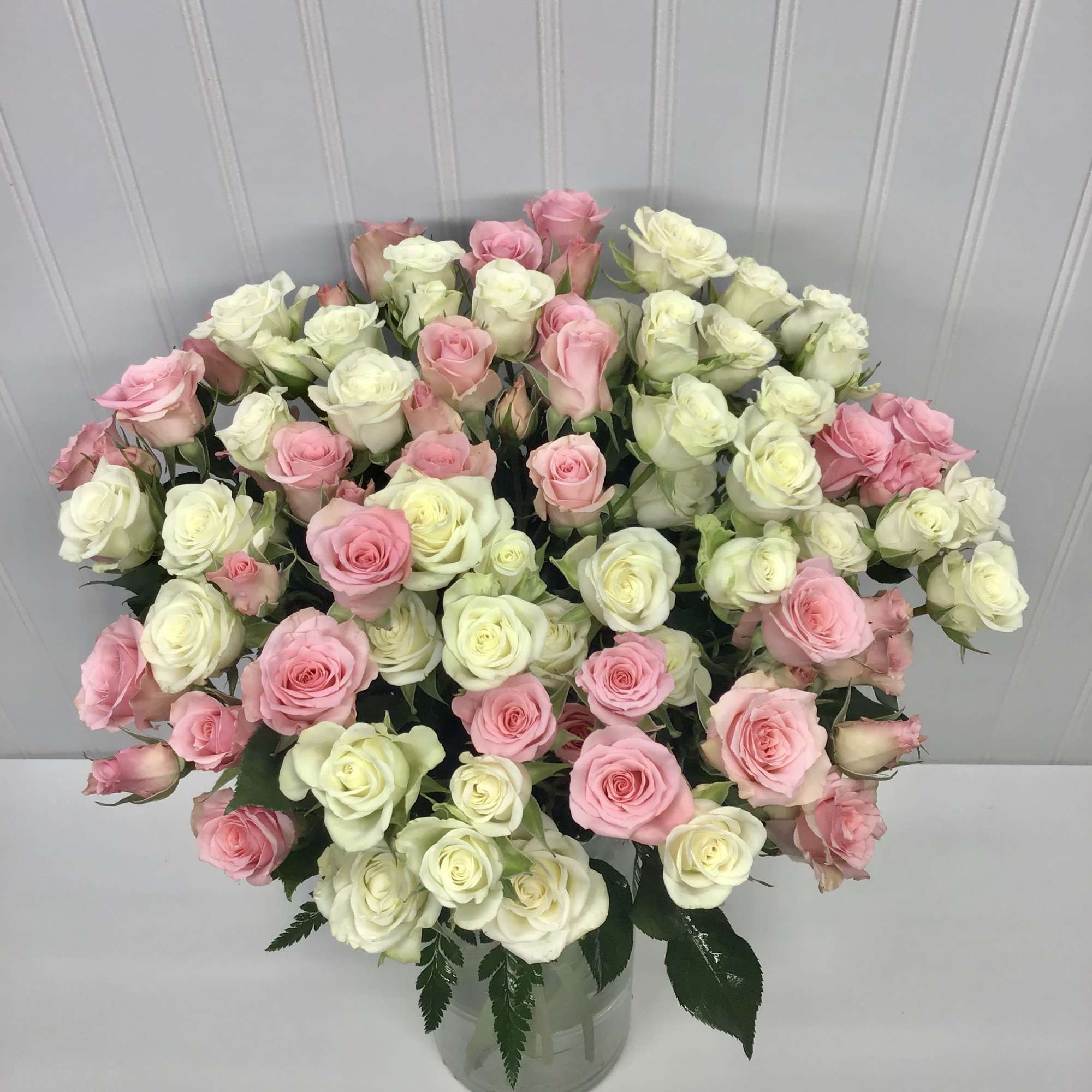 Large bouquet of white and soft pink roses arranged densely in a clear glass vase