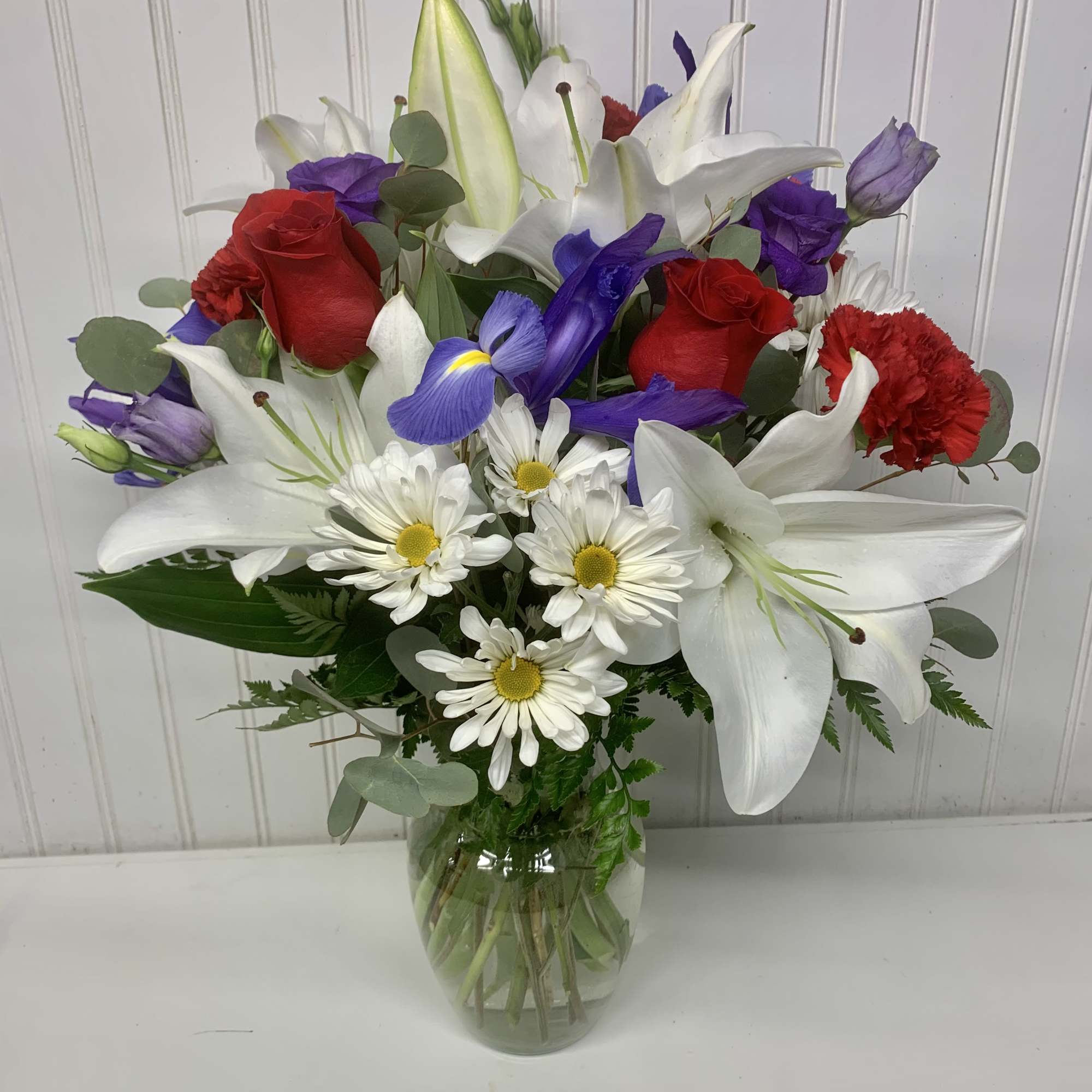 Mixed bouquet of red roses, white lilies, and daisies in a glass vase
