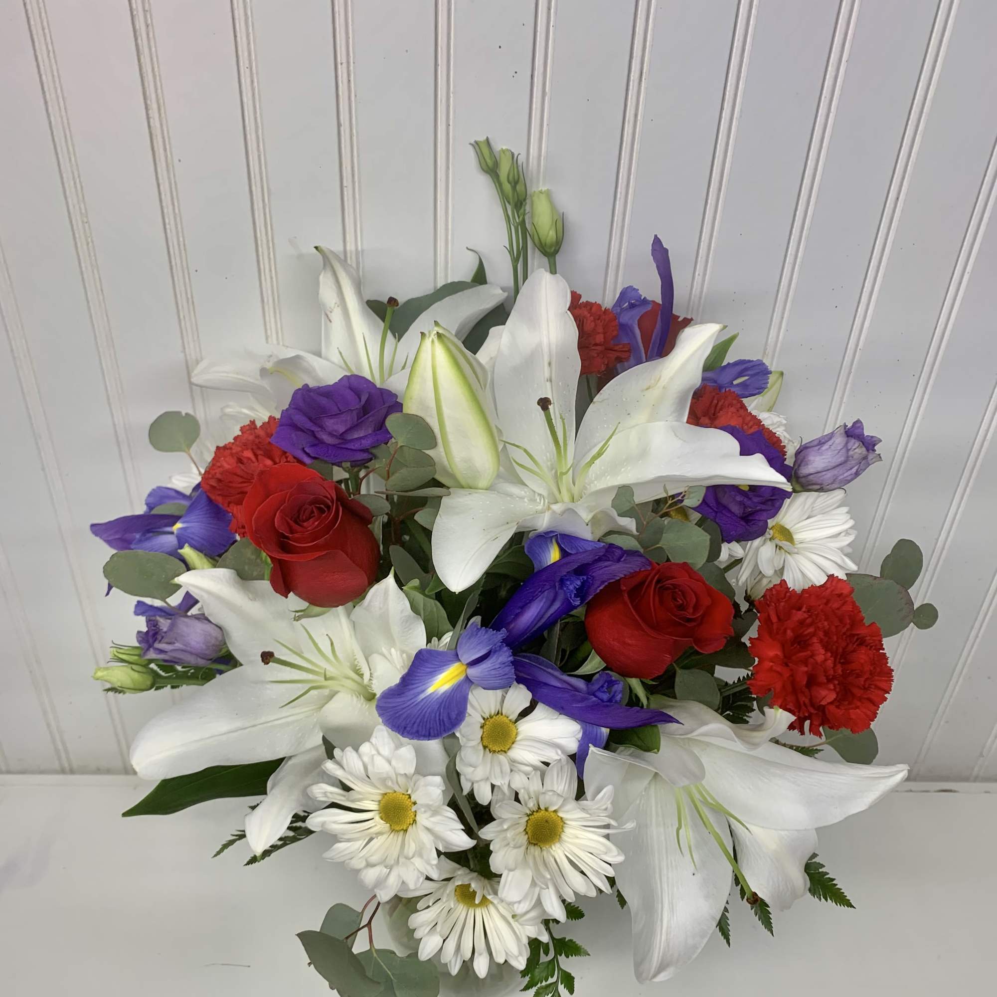 Mixed bouquet with white lilies, red roses, purple irises, and white daisies in a vase