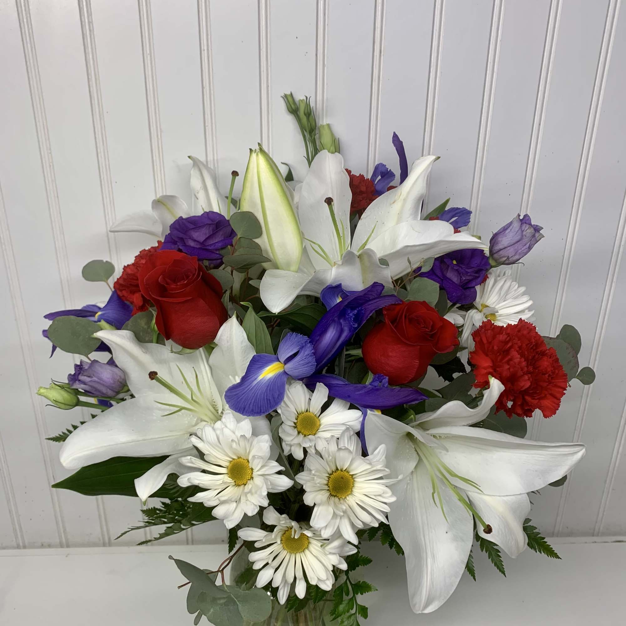 Bouquet of white lilies, red roses, purple iris, and white daisies in a glass vase