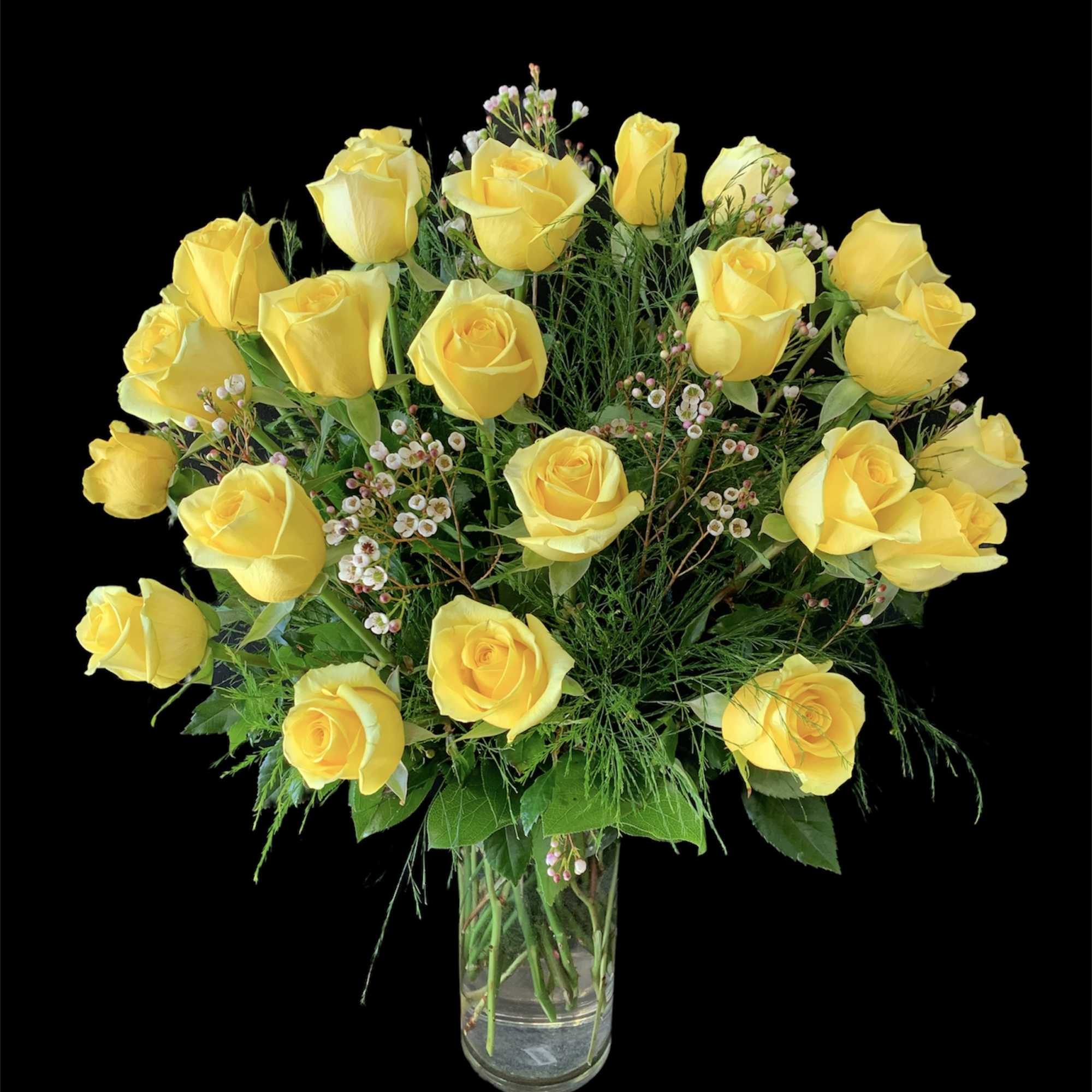 Arrangement of yellow roses with tiny white blooms in a clear glass vase