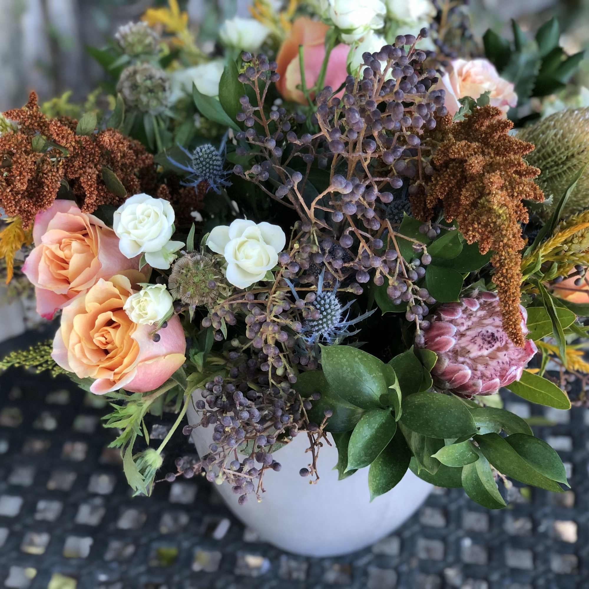 Mixed bouquet of peach roses and textured blooms in a white vase