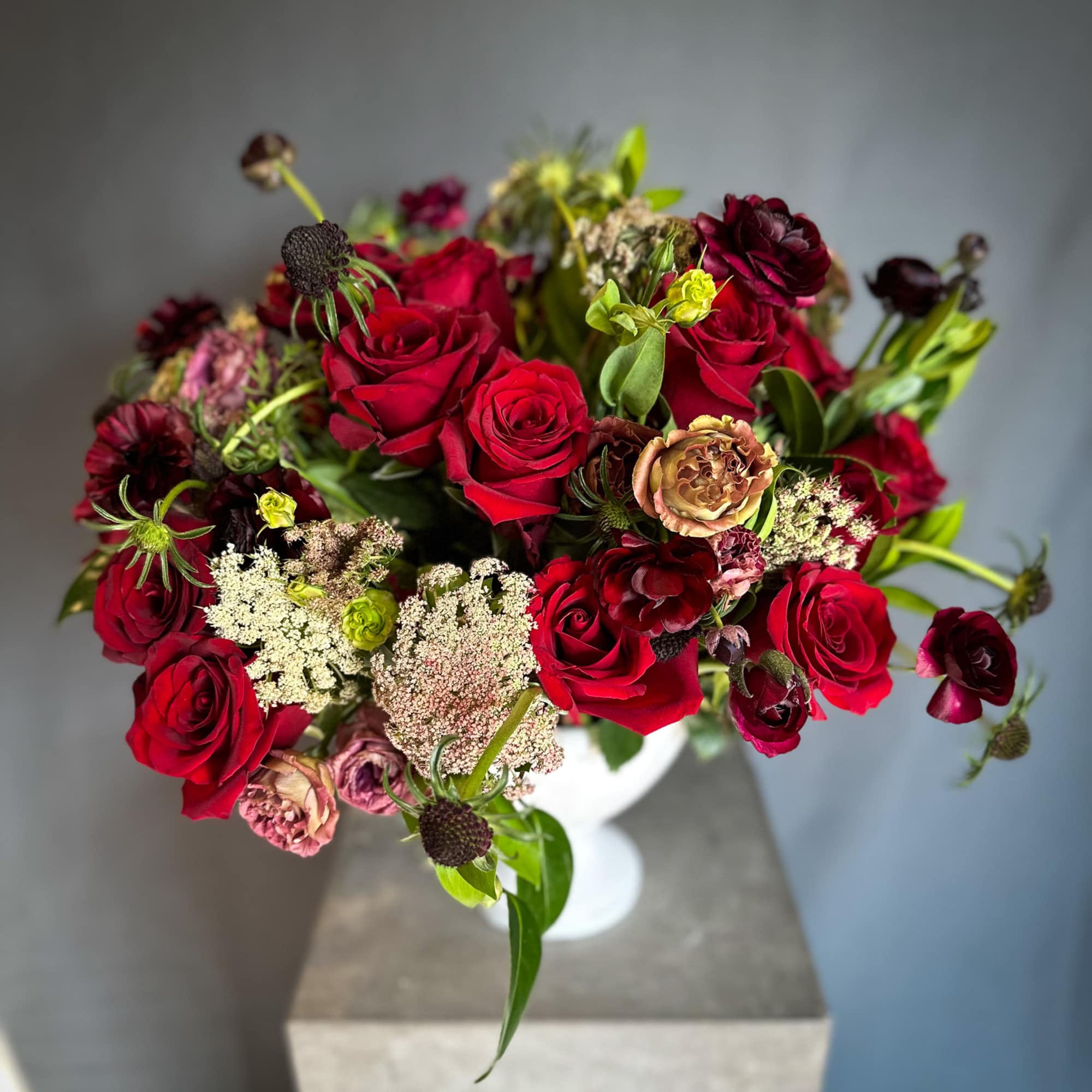 Bouquet of red roses and burgundy flowers in a white vase