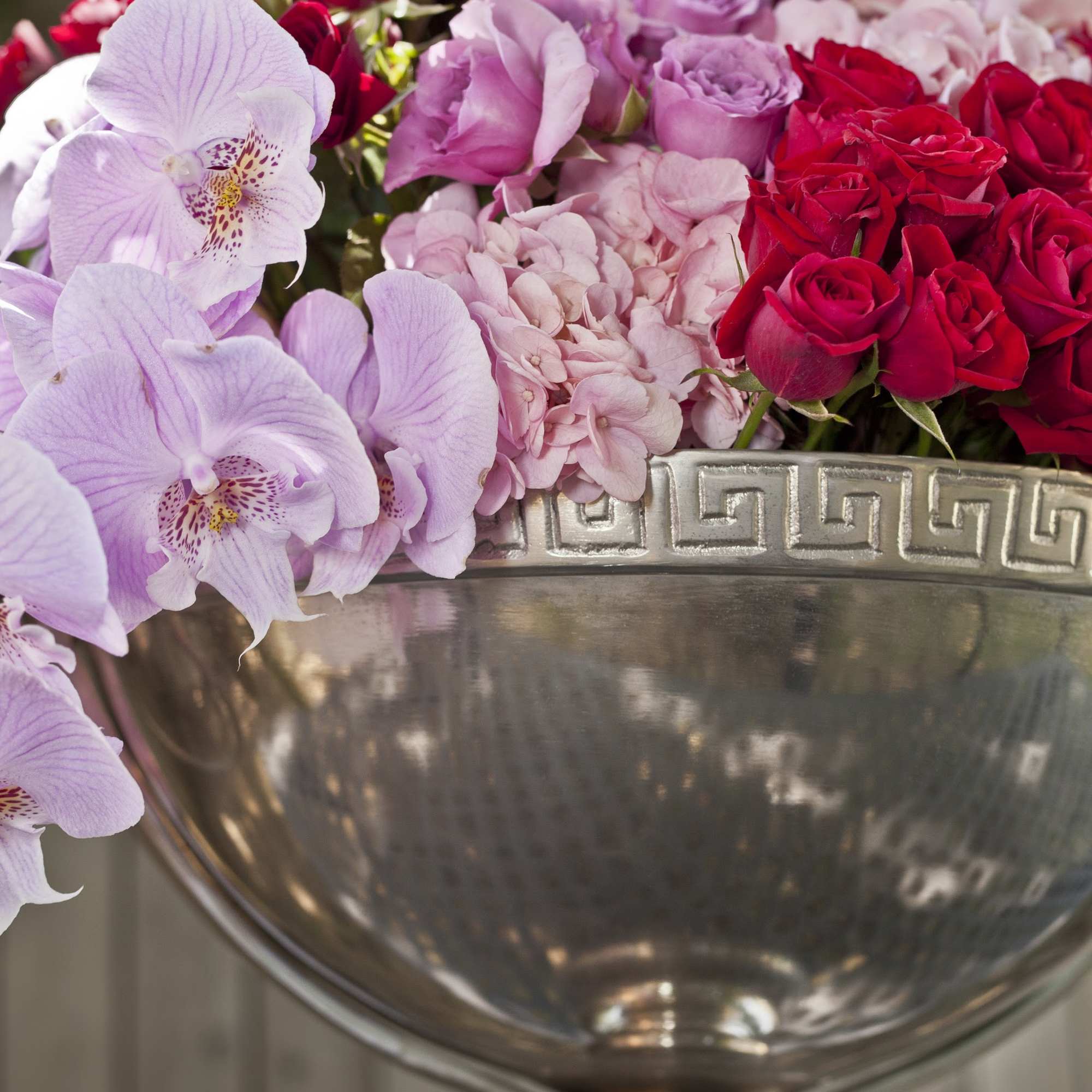 Pink and red roses with pale orchids in a silver vase