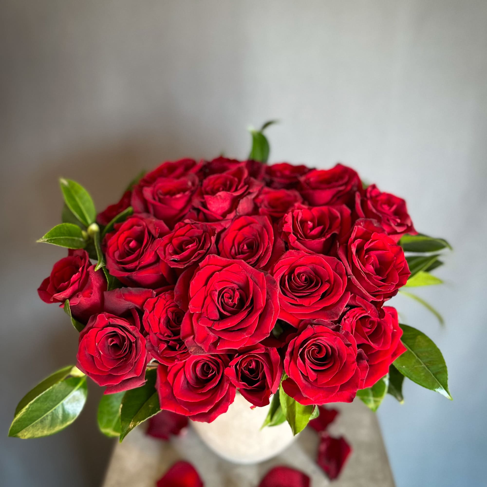 Bouquet of red roses in a white vase with scattered petals