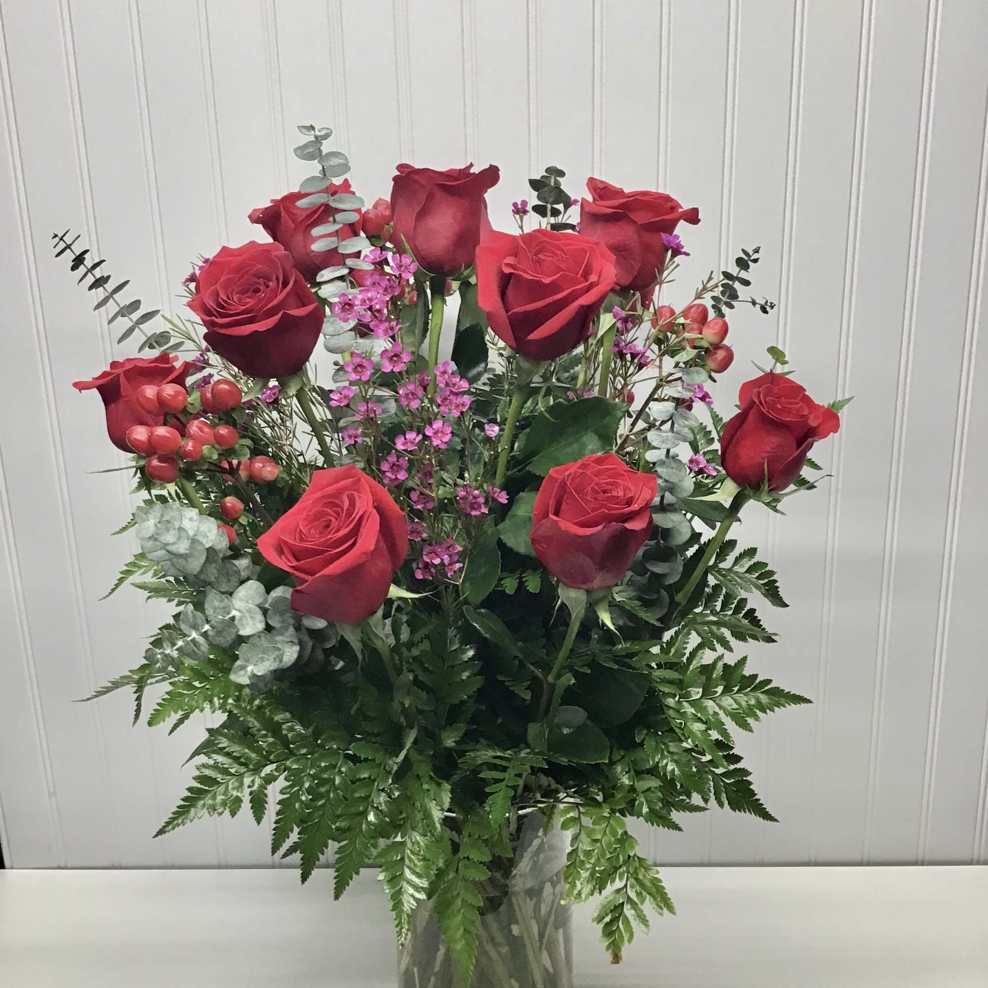 Tall arrangement of red roses with small pink blooms in a clear glass vase