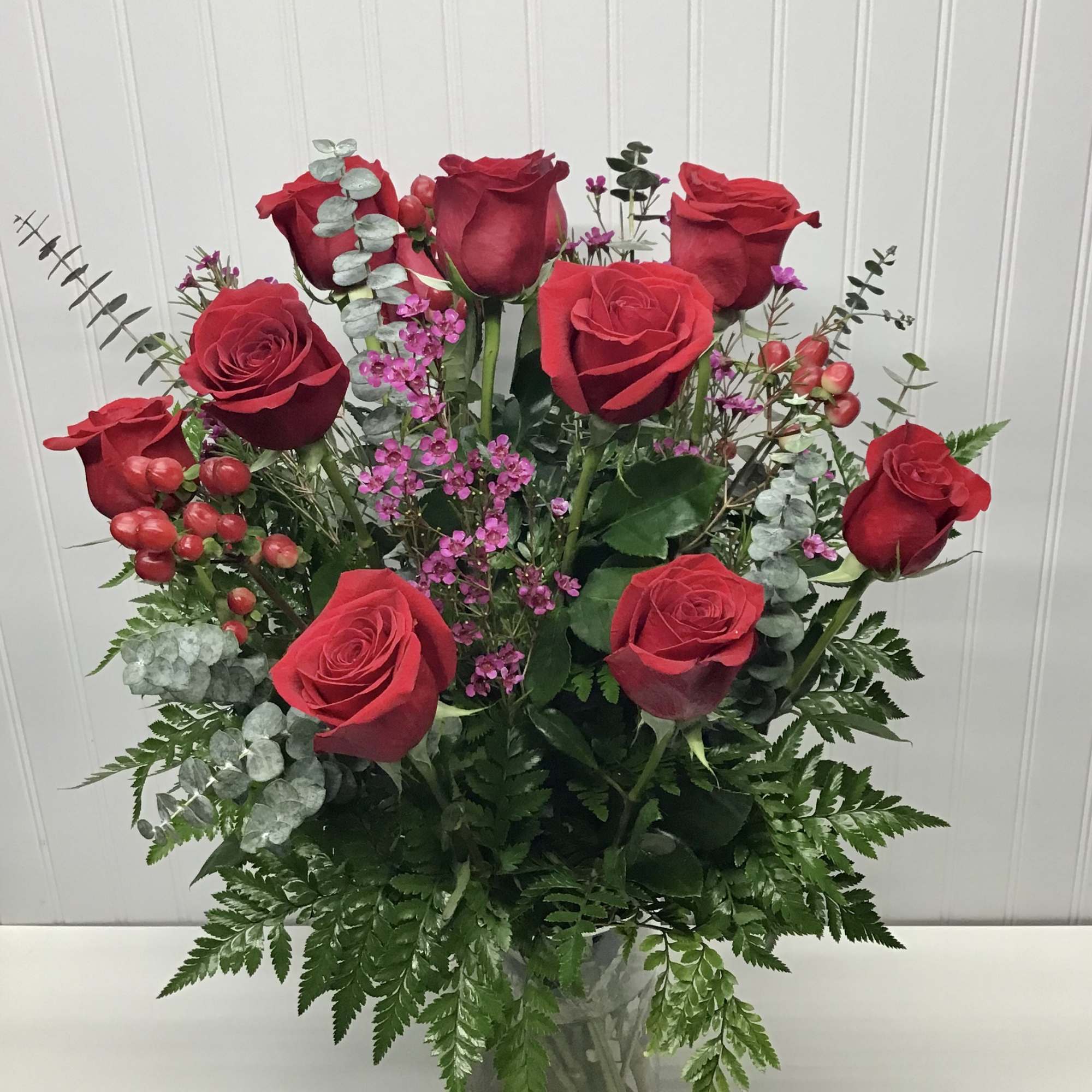 Tall arrangement of red roses with small pink flowers in a clear glass vase