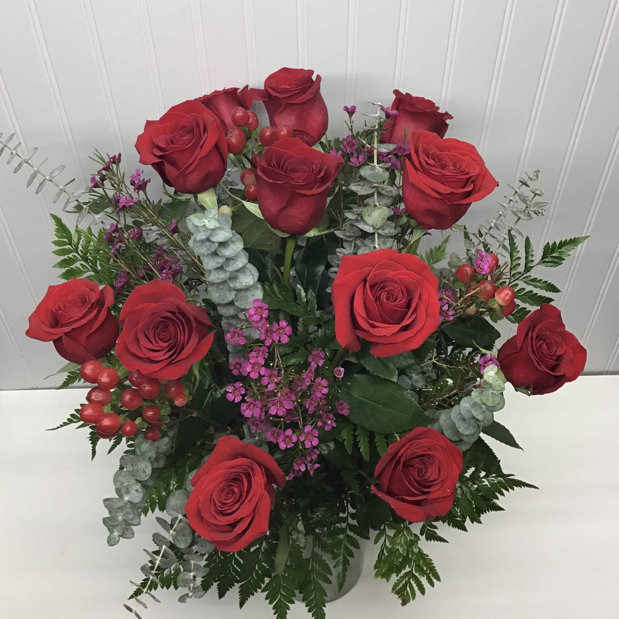 Arrangement of red roses with small purple blooms in a clear glass vase