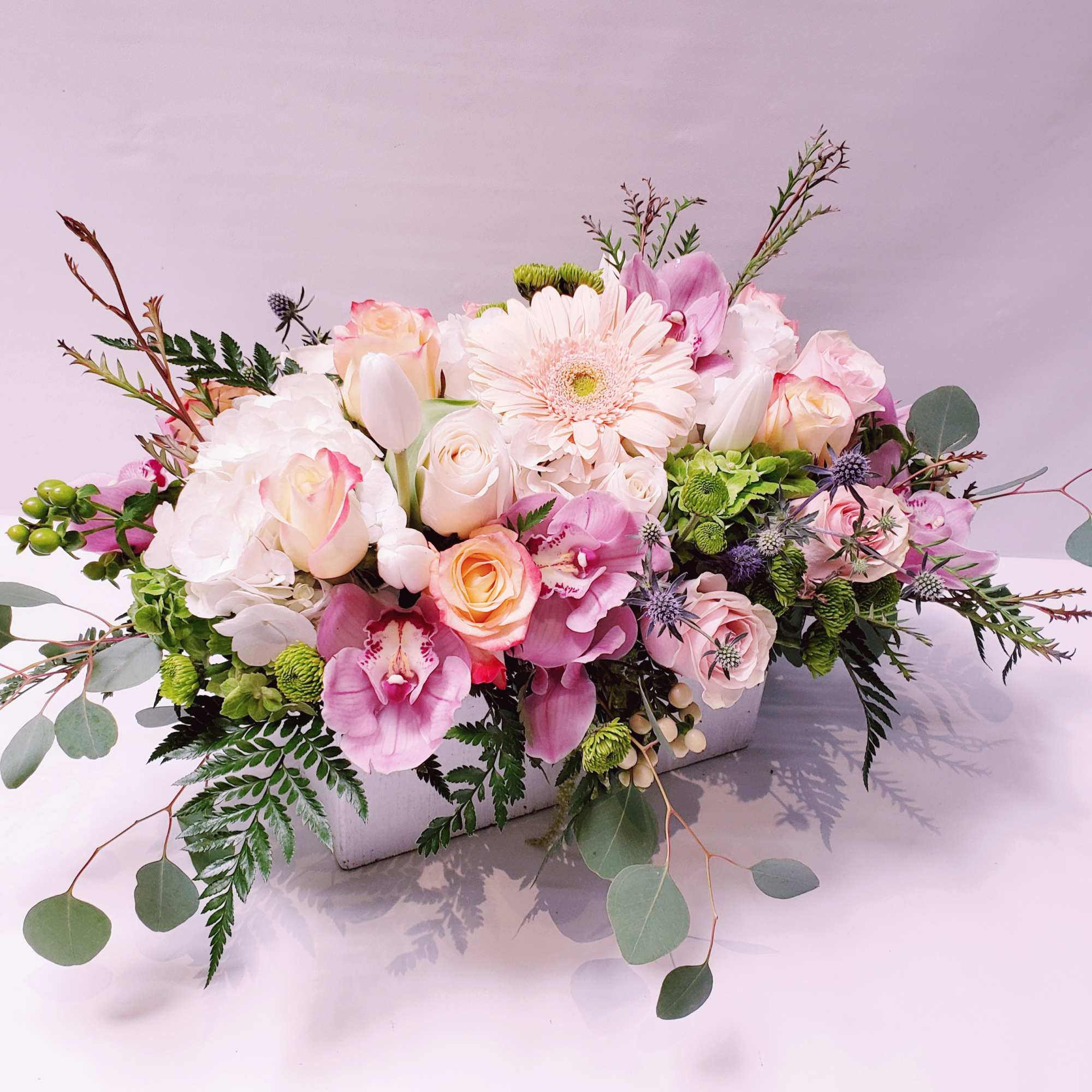 Low pastel arrangement of roses, orchids, hydrangea, tulips, and gerbera in a white rectangular container