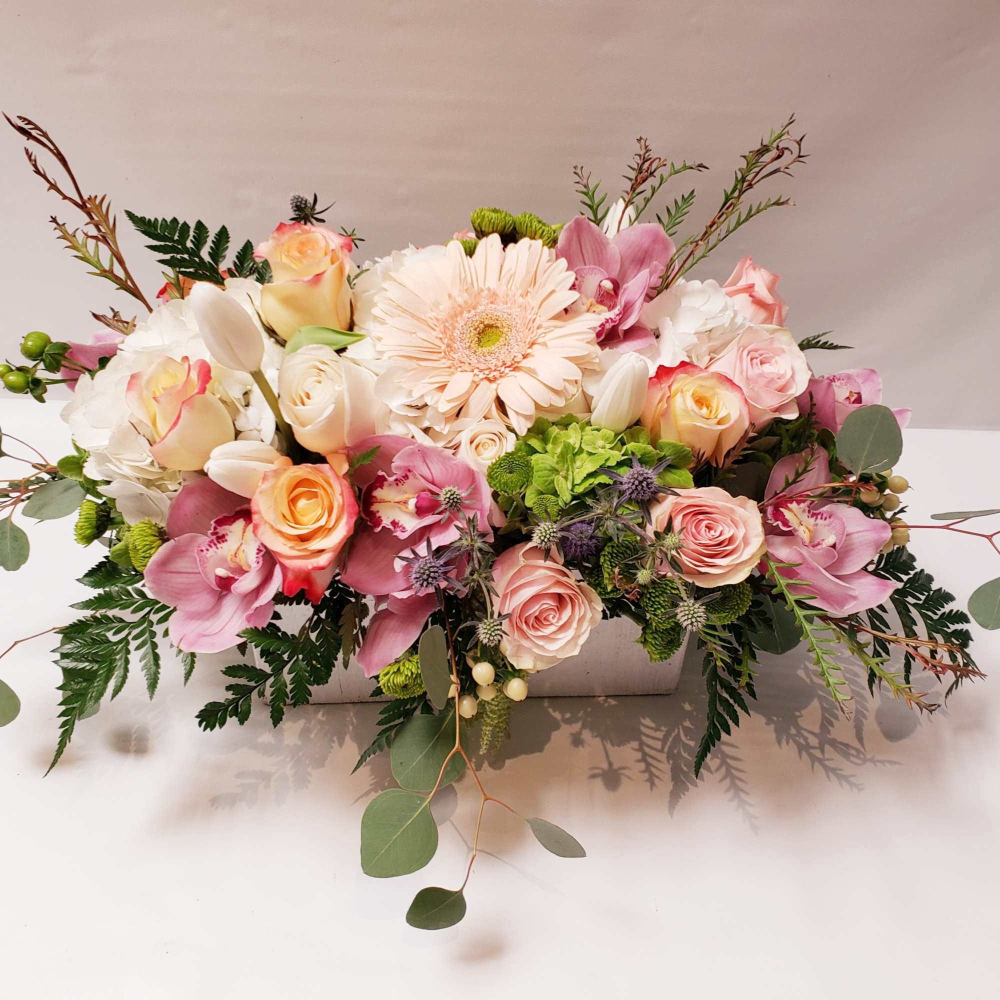 Low pastel arrangement of roses, gerbera daisy, orchids, tulips and hydrangea in a white rectangular container