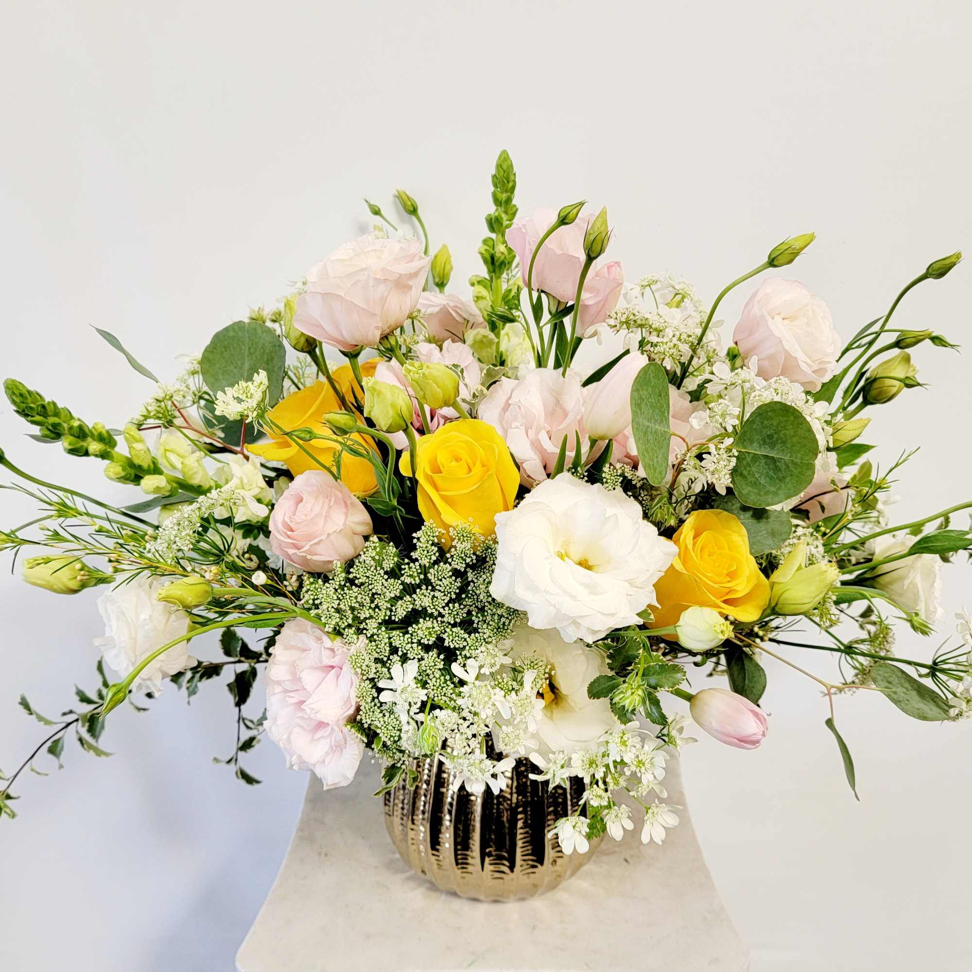 Mixed bouquet of yellow, white, and pale pink flowers in a gold vase