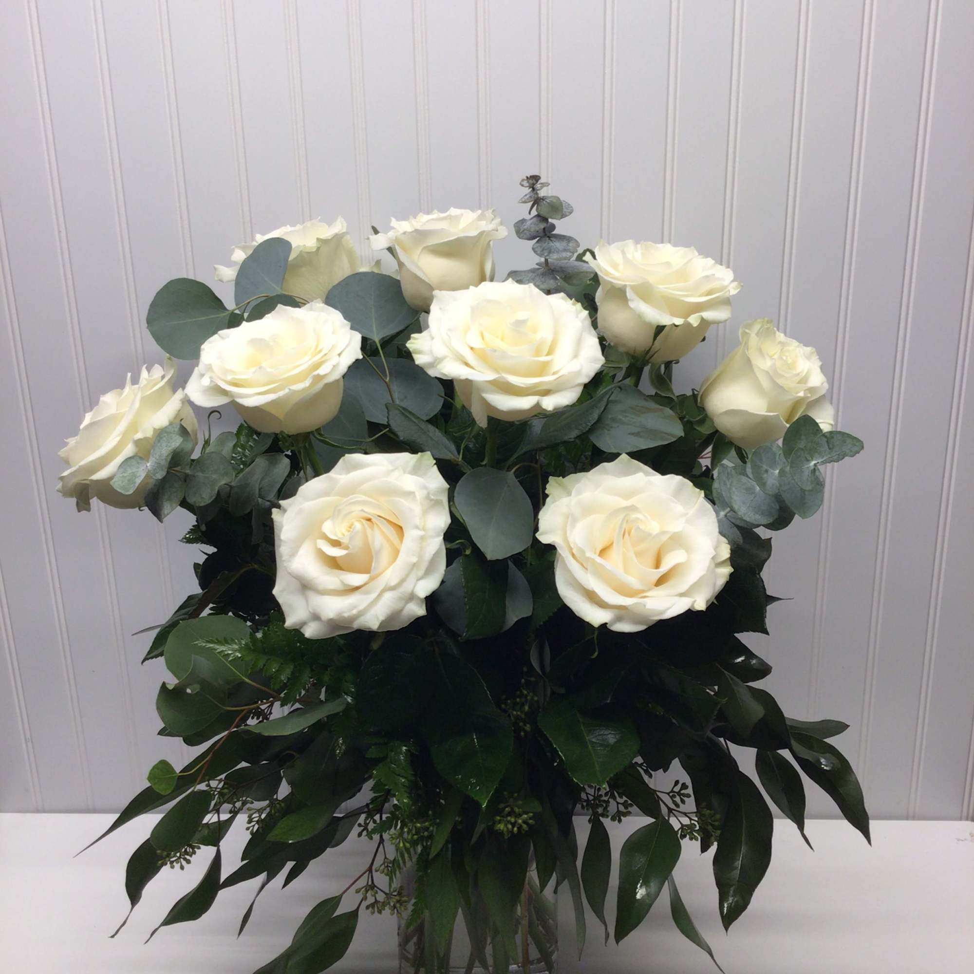 Tall arrangement of ivory roses with abundant greenery in a clear glass vase