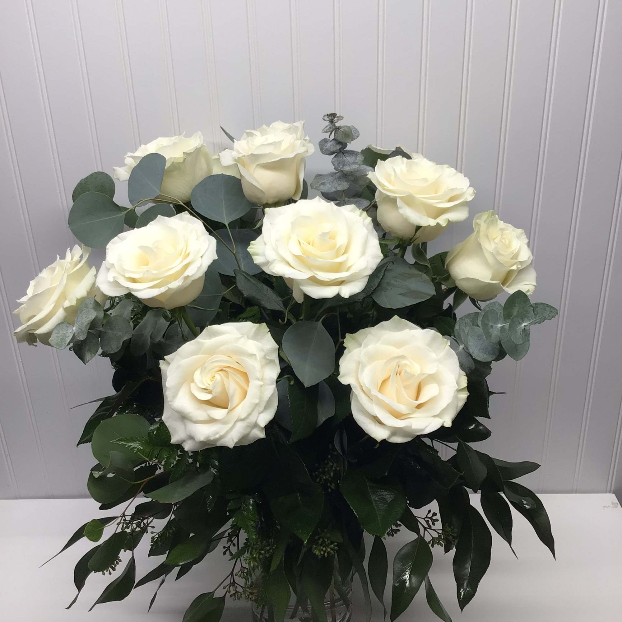 Arrangement of large white roses in a clear glass vase with lush greenery.