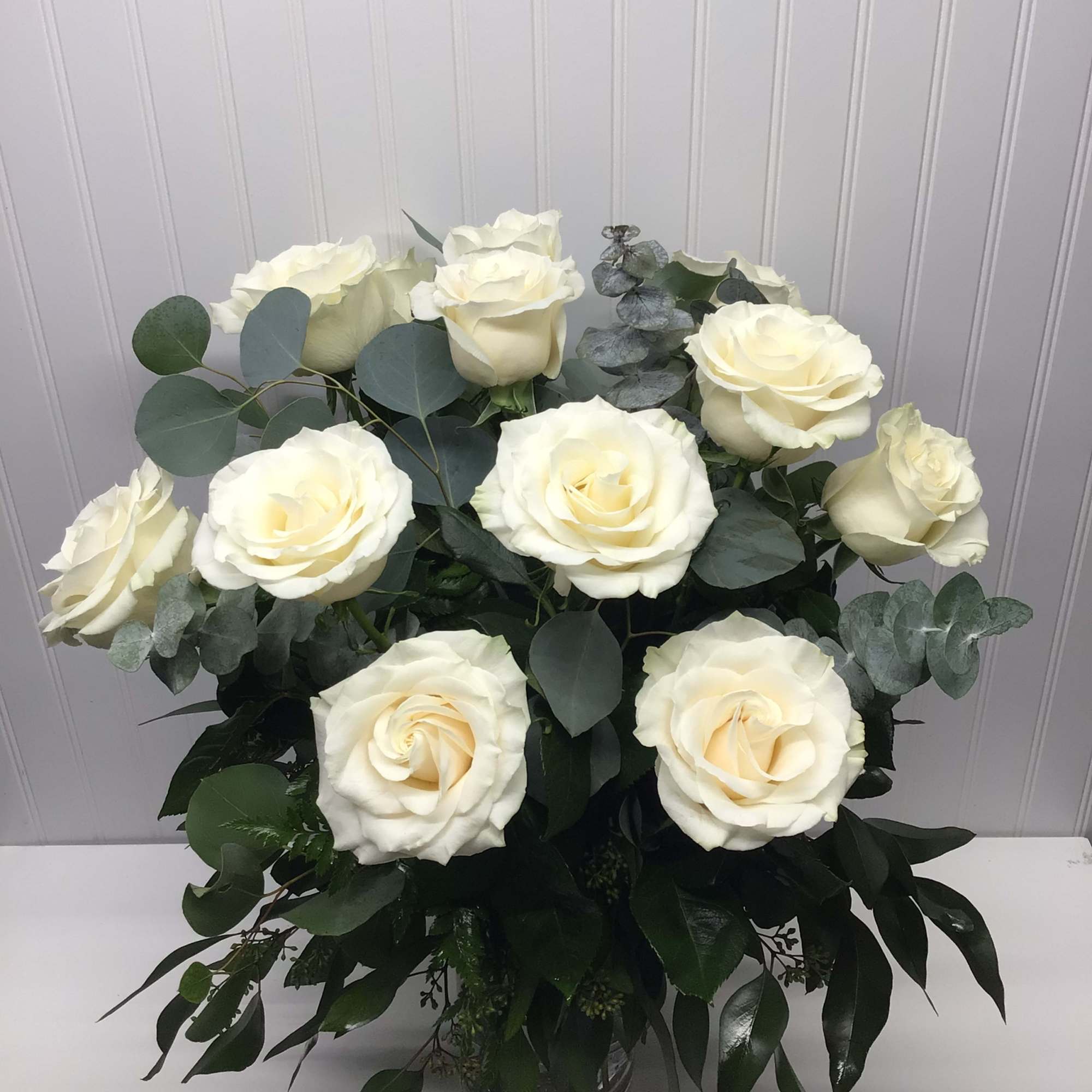 Arrangement of large ivory roses with abundant greenery in a clear glass vase