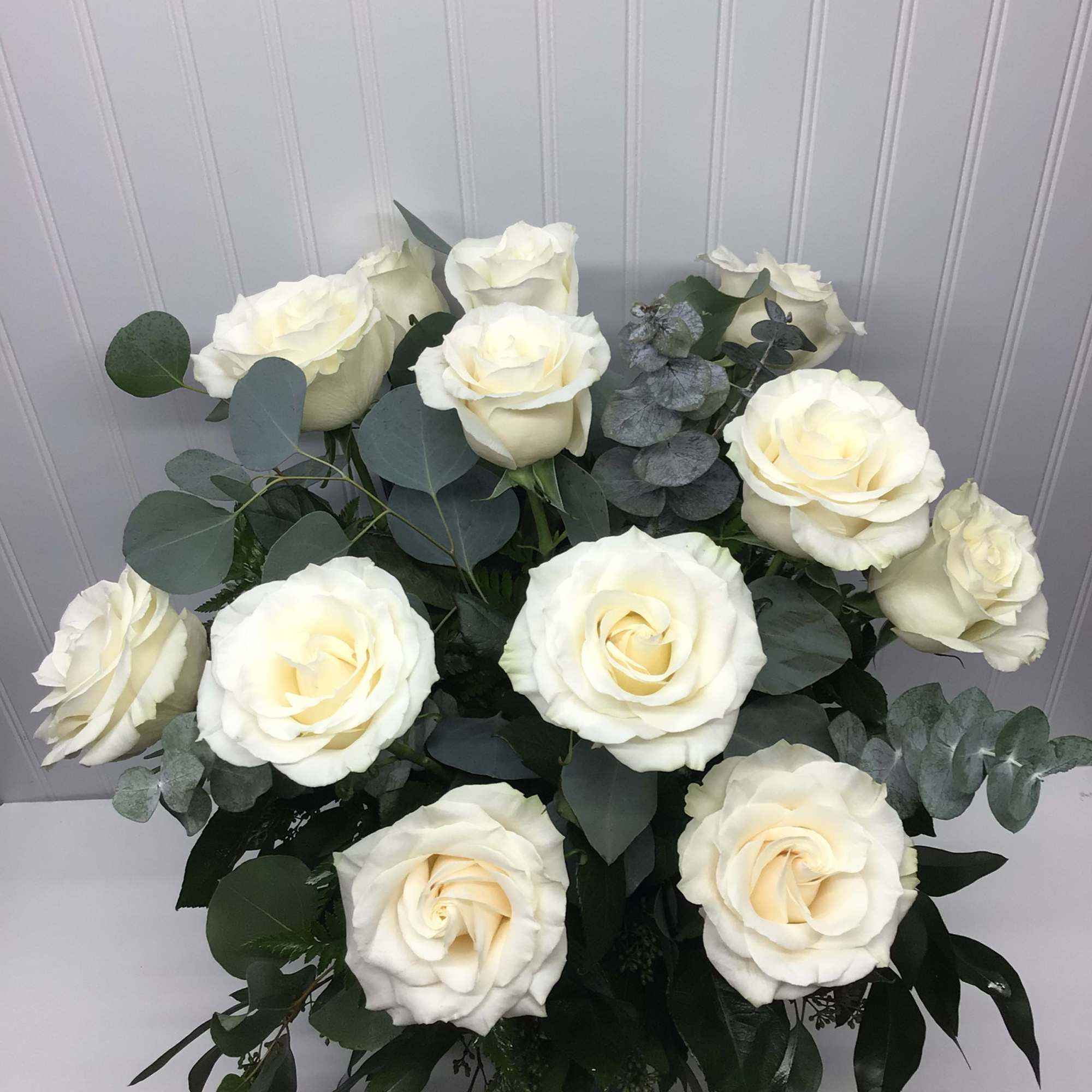 Arrangement of large ivory roses with silver eucalyptus in a rounded design