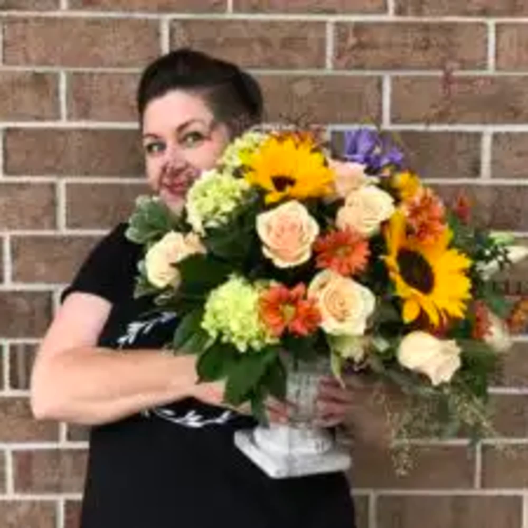 Woman holding a mixed bouquet with sunflowers and roses in a white vase