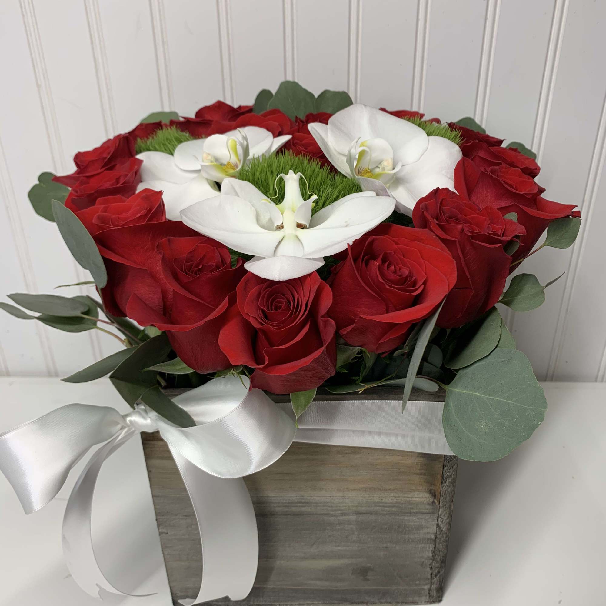 Low arrangement of red roses with white orchids in a rustic wooden box tied with a white ribbon.