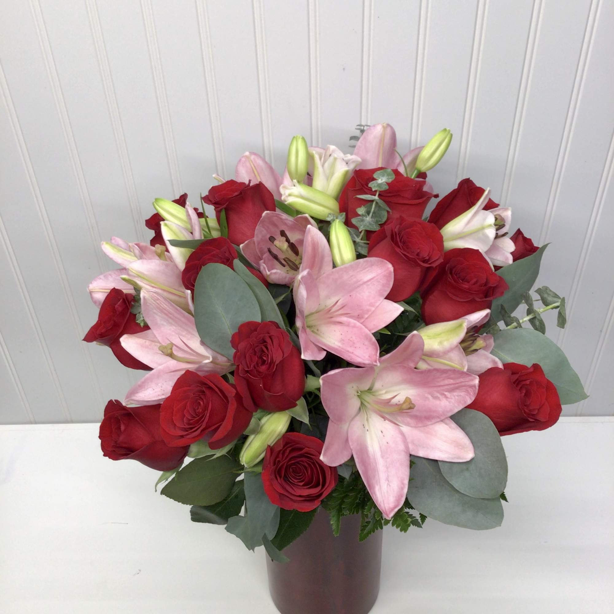 Arrangement of red roses and pink lilies in a tall red glass vase