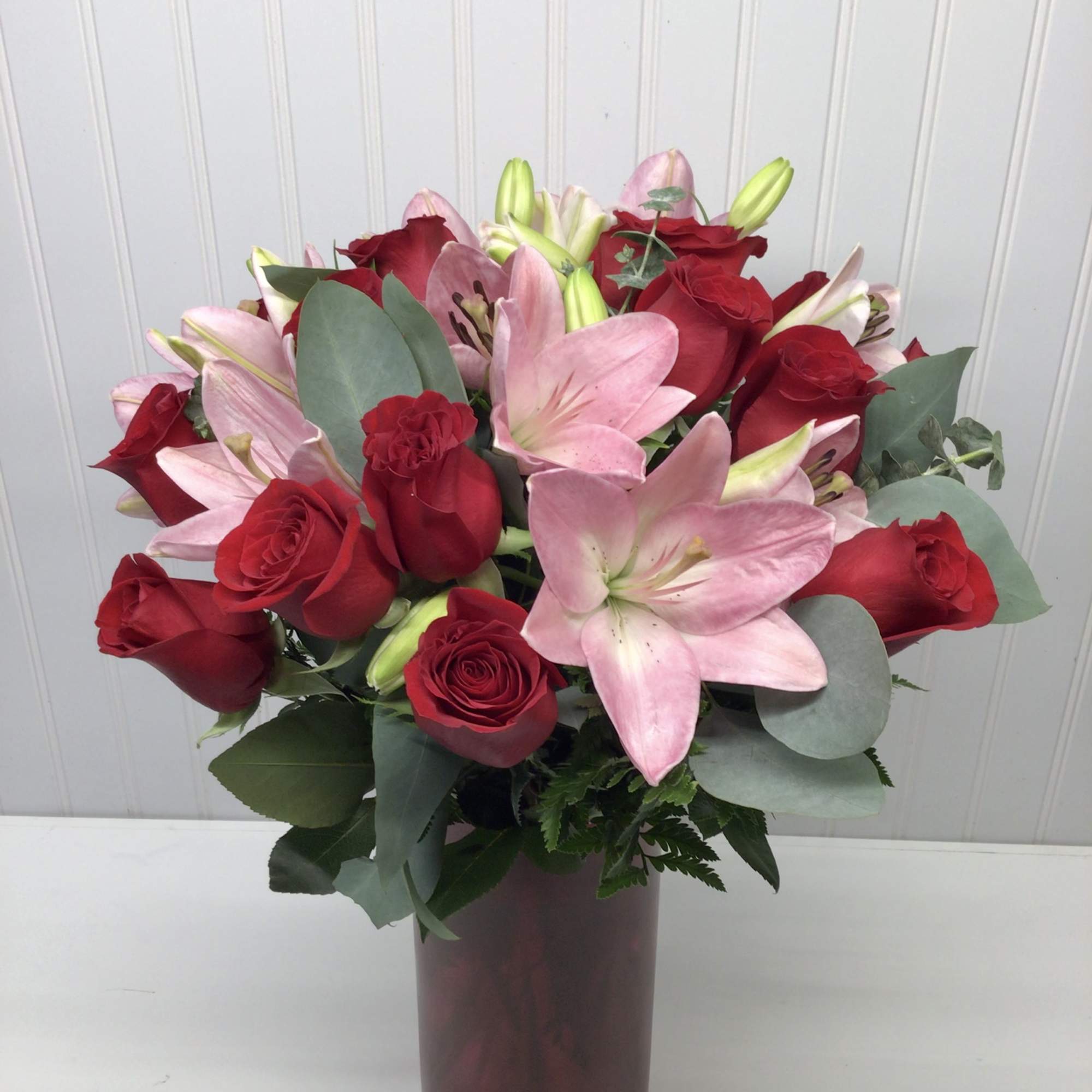 Arrangement of red roses and pink lilies in a tall red vase