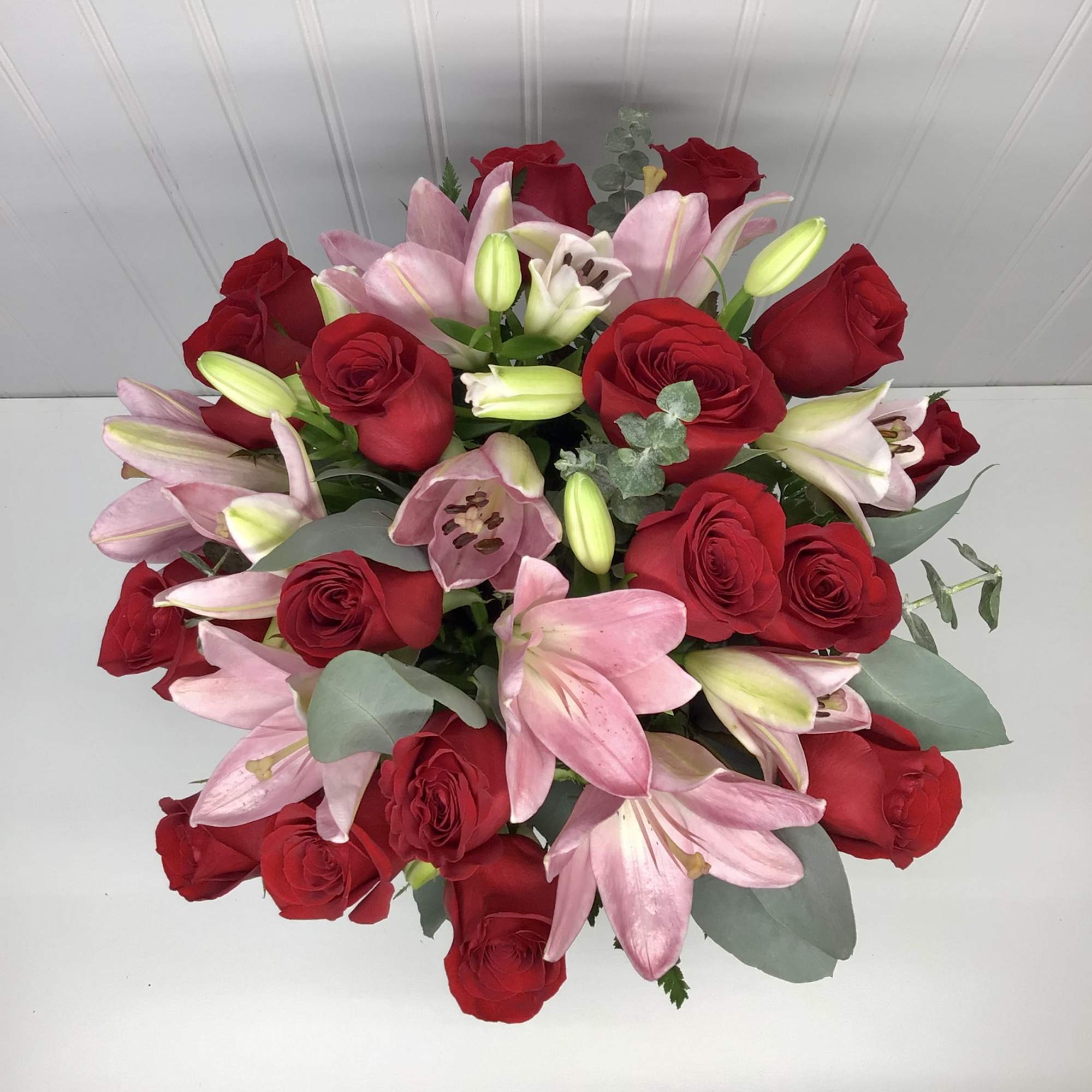 Round arrangement of red roses and pink lilies viewed from above on a light background