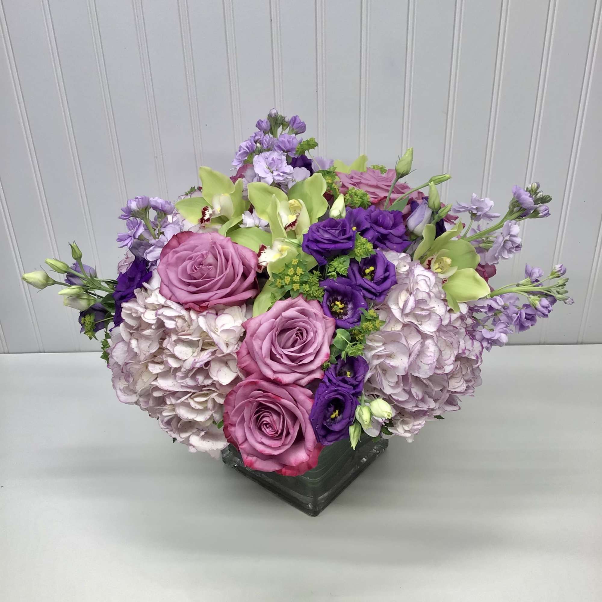 Bouquet of pink and purple flowers with green orchids in a low vase