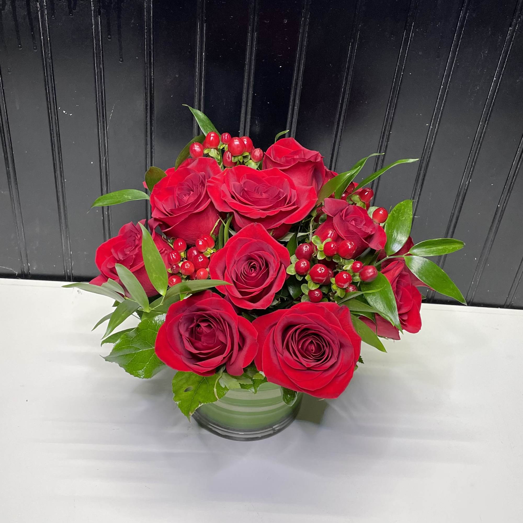 Red roses arranged in a clear glass vase with red berries