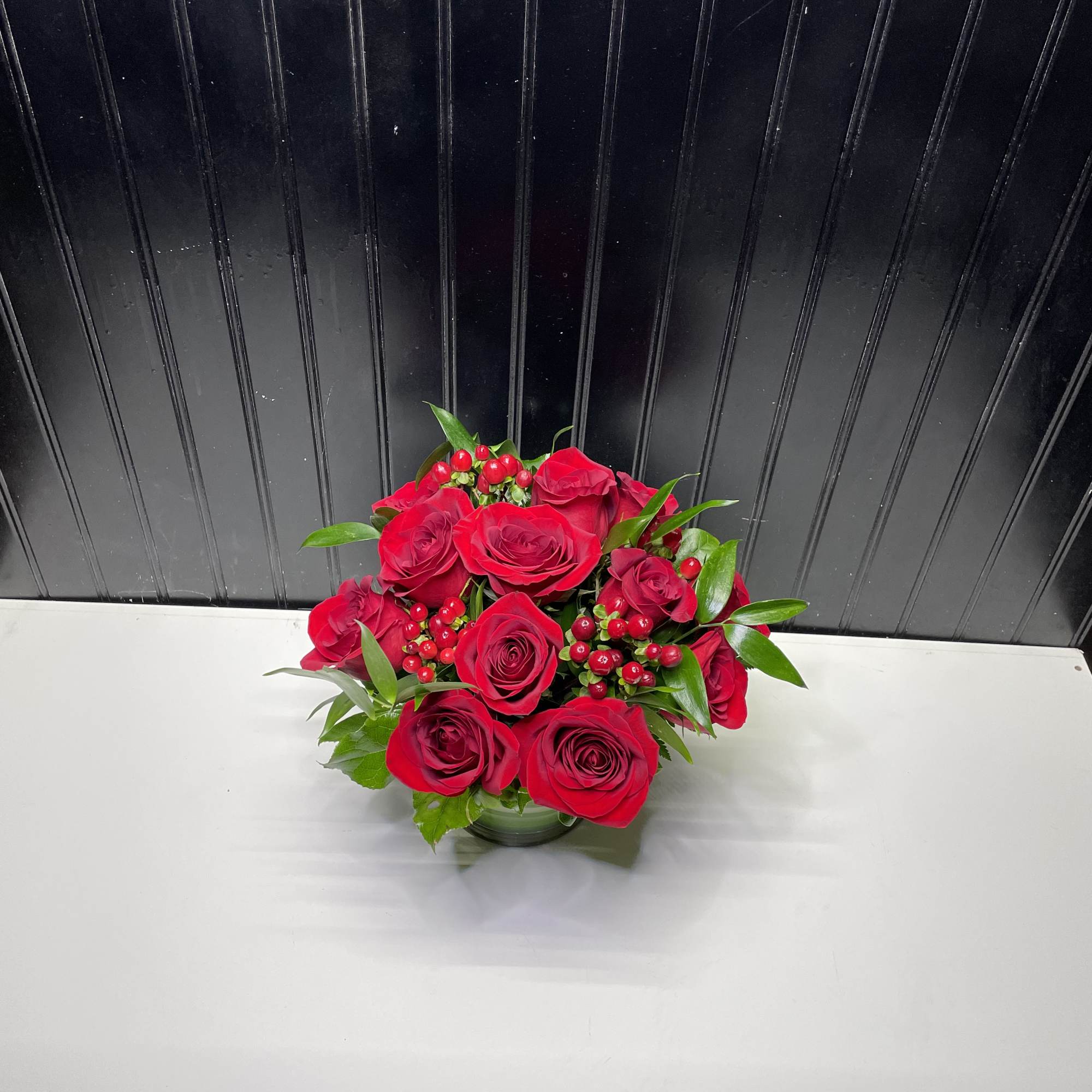 Red rose bouquet in a low glass vase with berry accents