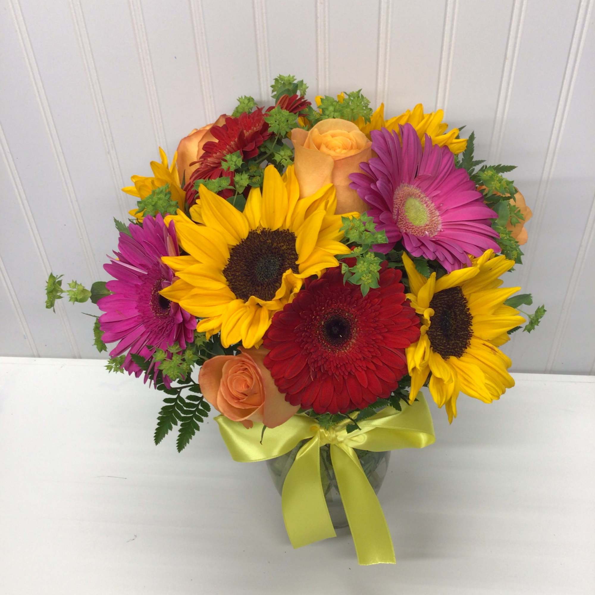 Bouquet of sunflowers, gerbera daisies, and roses in a glass vase with a yellow ribbon
