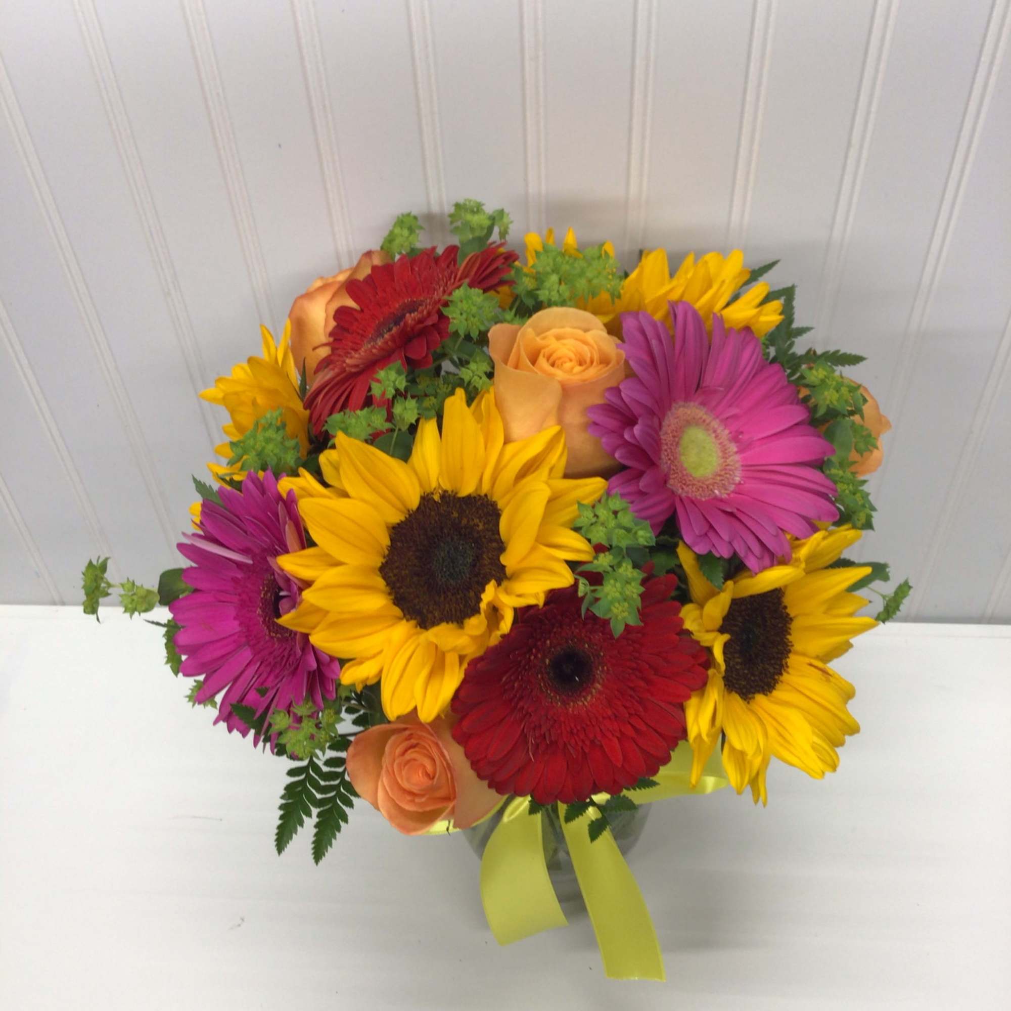 Bouquet of sunflowers, gerbera daisies, and roses in a glass vase